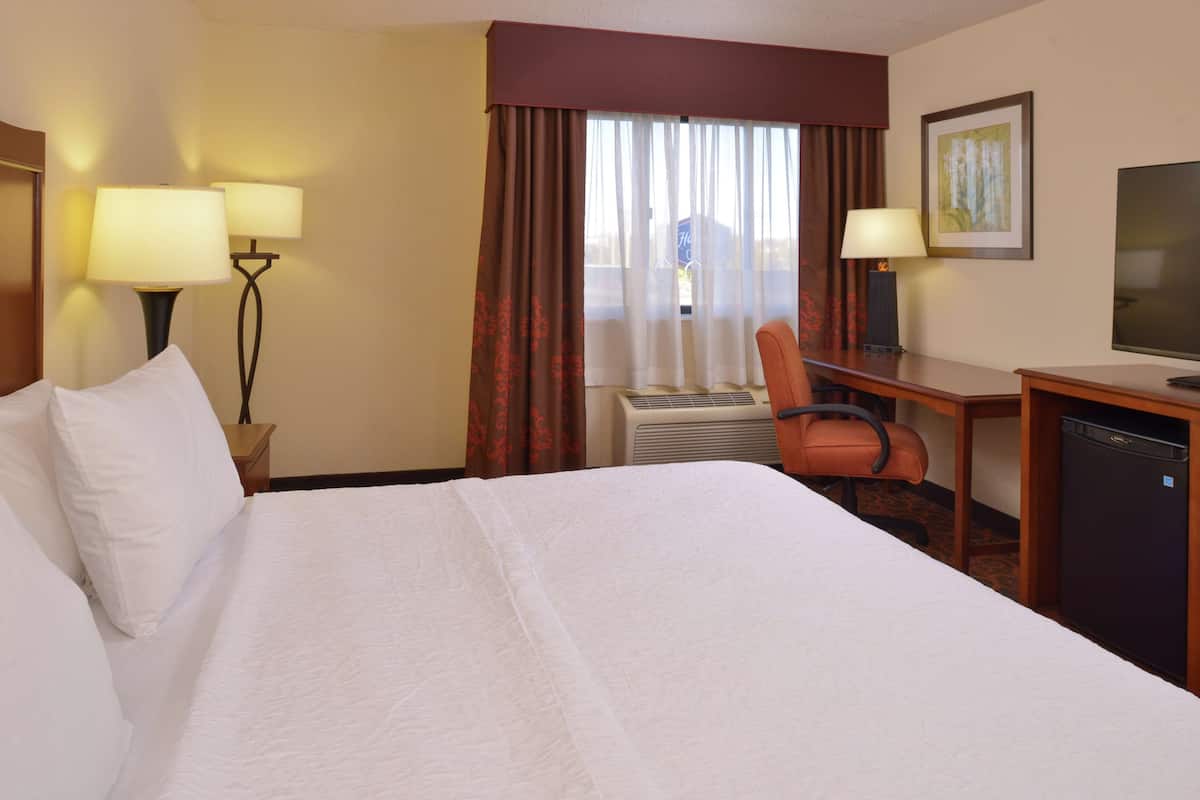 A hotel room with a large bed, a desk with a chair, a television, and a small refrigerator.
