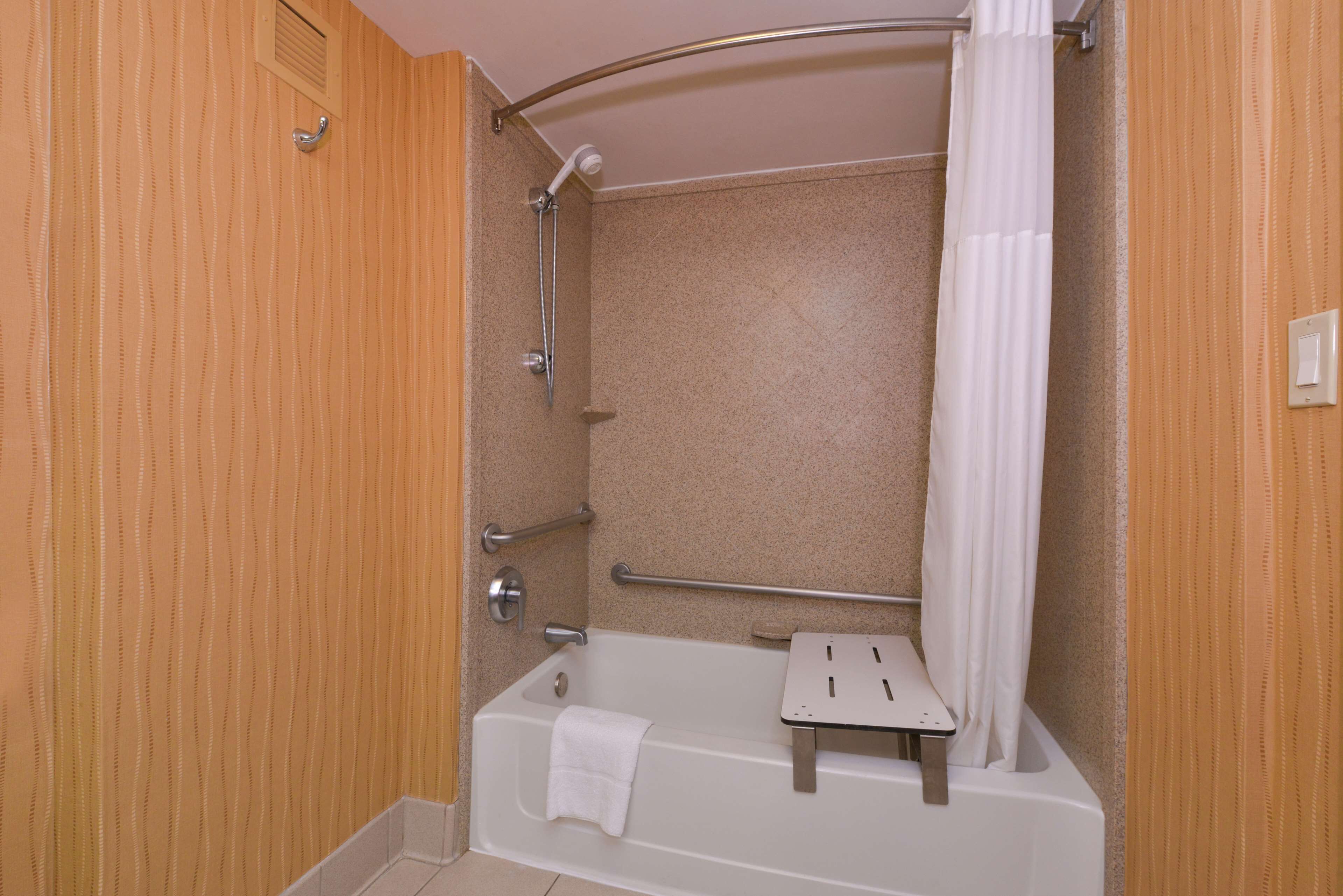 Een badkamer met een bad, een douche, een handgreep en een handdoekhouder.