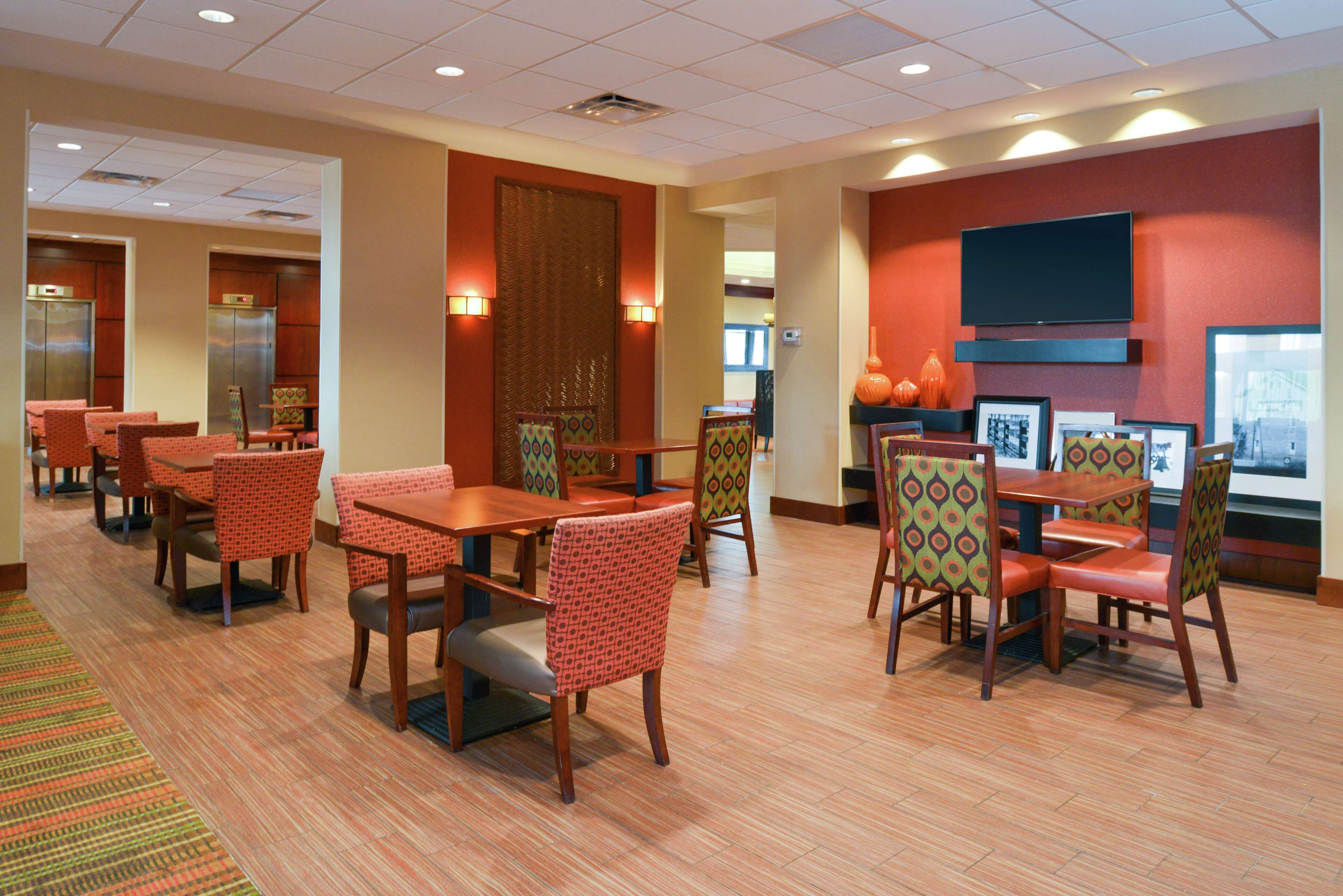 A hotel dining area with multiple tables and chairs, a television mounted on the wall, and a fireplace.