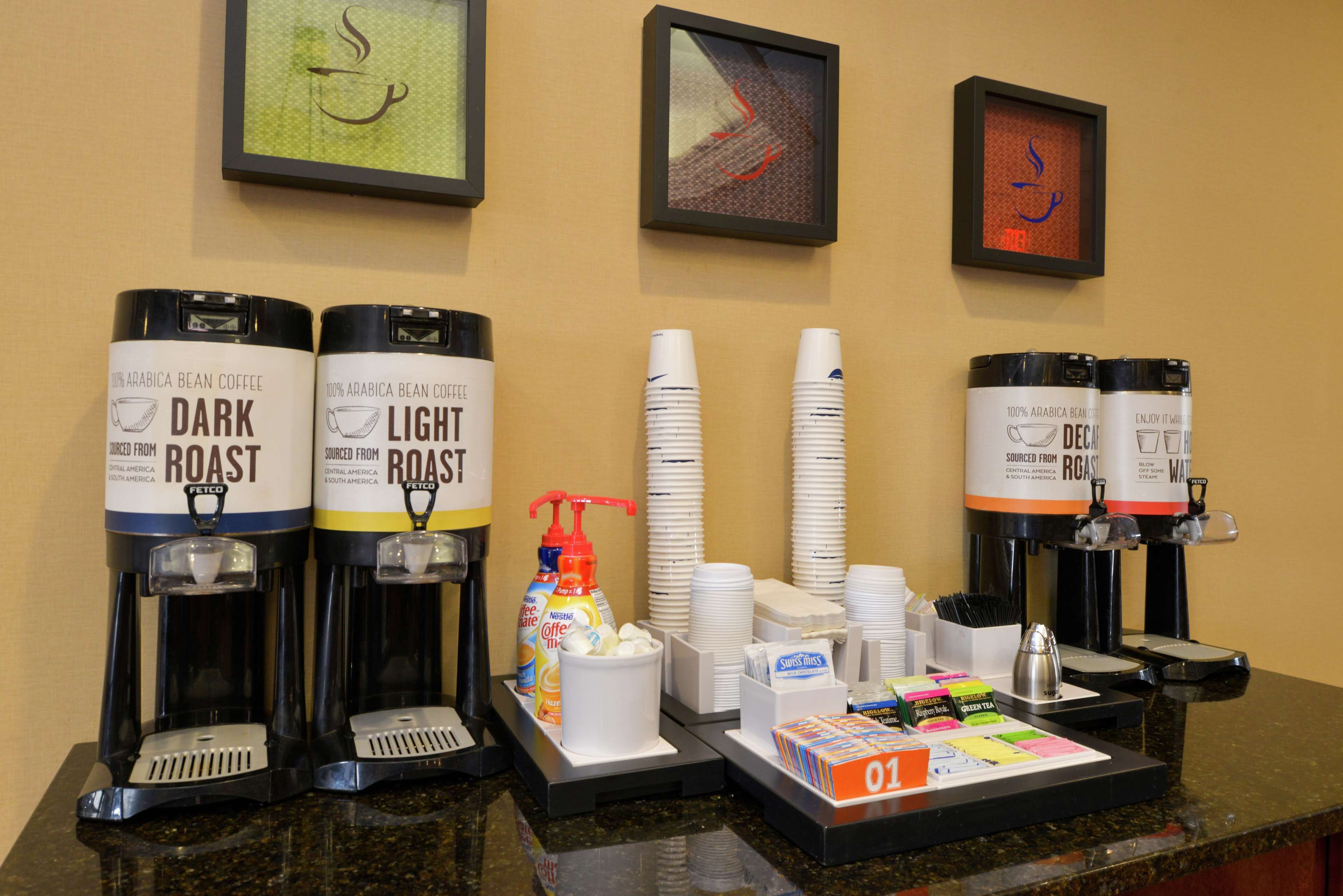 Una estación de café con dos dispensadores de café, uno con café tostado oscuro y otro con tostado claro, una pila de vasos desechables y un molinillo de café.