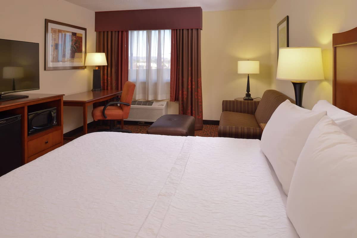 A hotel room with a large bed, a desk with a chair, a television, and two lamps.