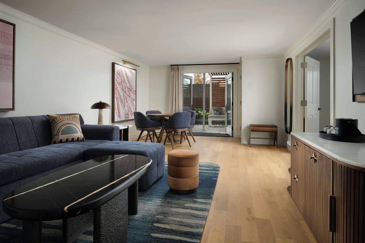 Ein modernes Wohnzimmer mit Sofa, Couchtisch und Sesseln. Ein Schiebeglastür führt auf einen Balkon.