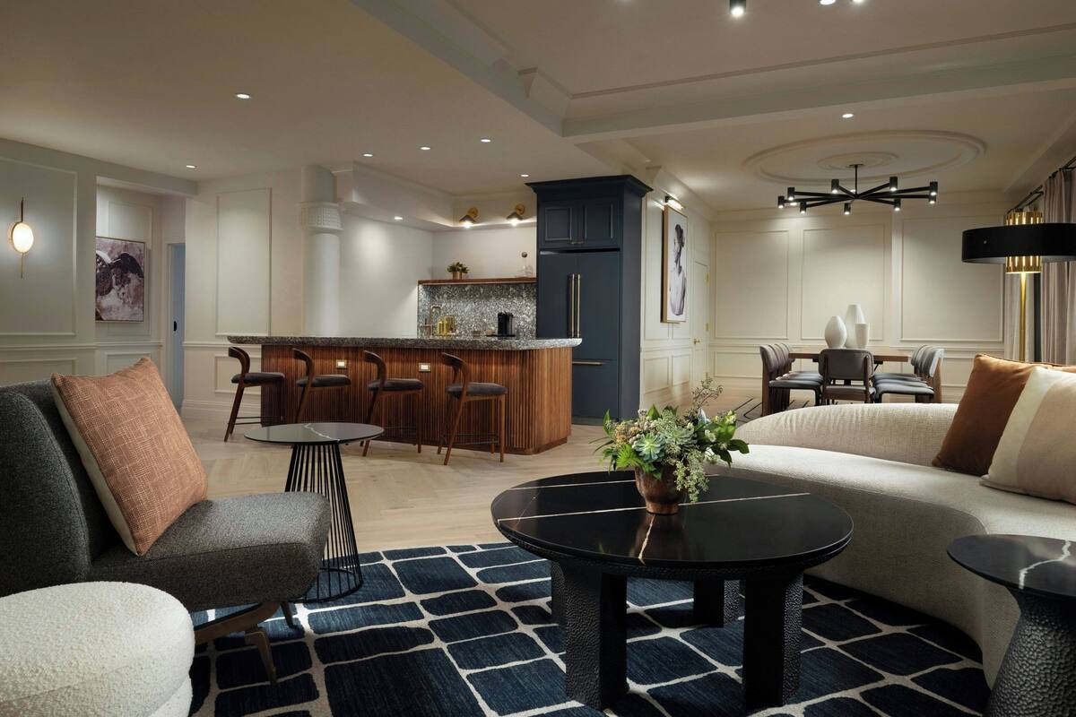 Ein modernes Wohnzimmer mit einer Couch, einem Couchtisch und einem Essbereich mit Stühlen sowie einer kleinen Küche im Hintergrund.