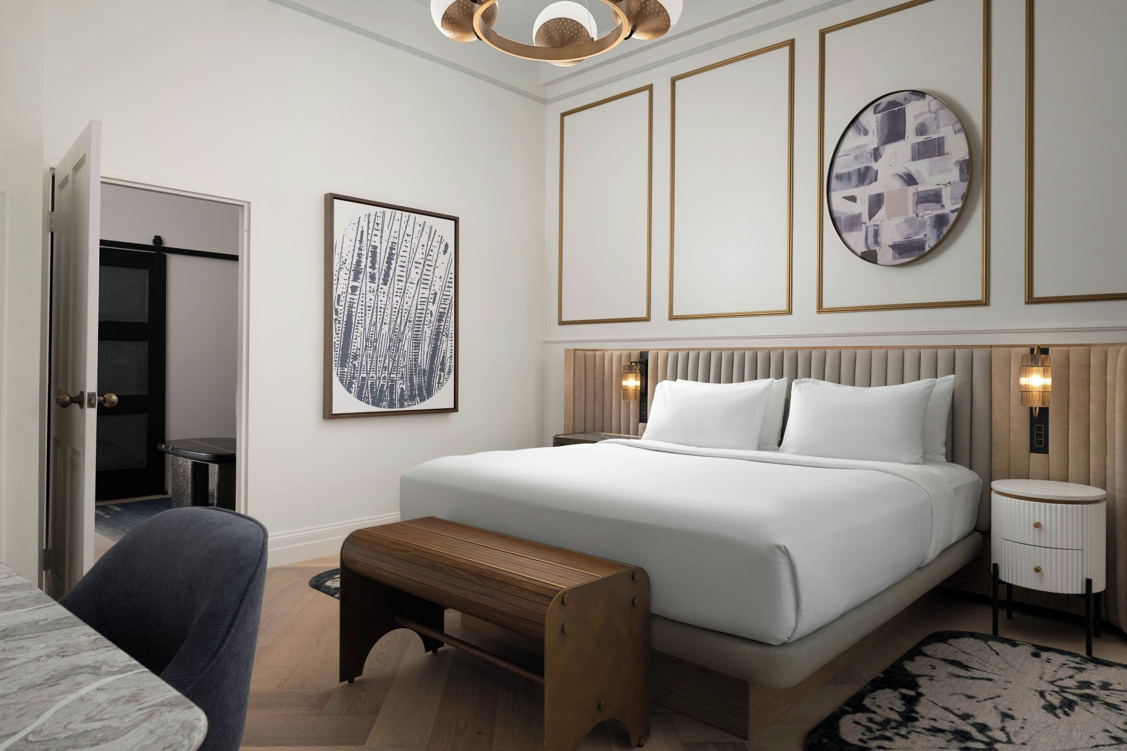 Un dormitorio moderno con una cama grande, mesitas de noche, un banco y obras de arte en las paredes.