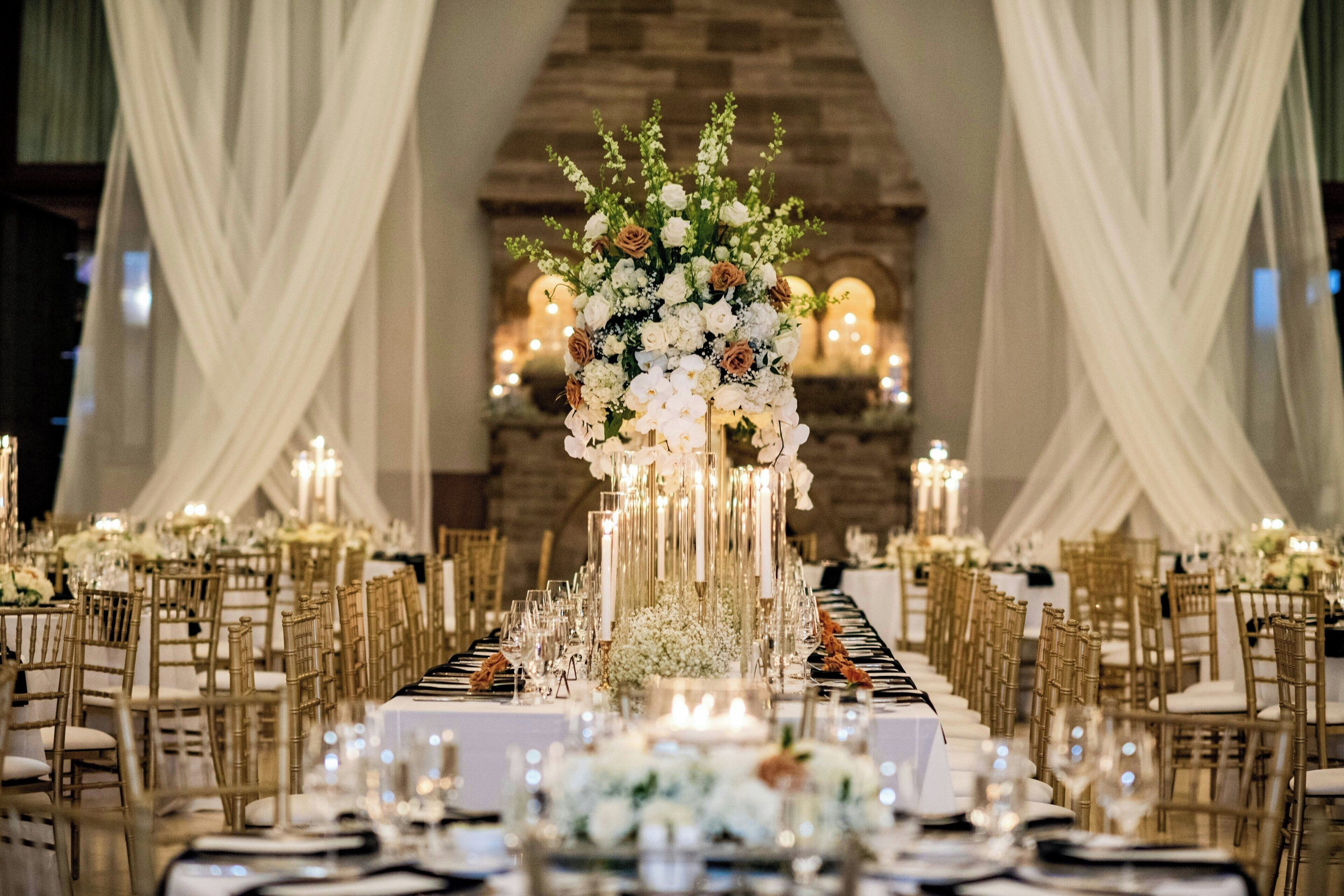 Une salle de banquet avec de longues tables, des tentures blanches et des centres de table illuminés par des bougies.