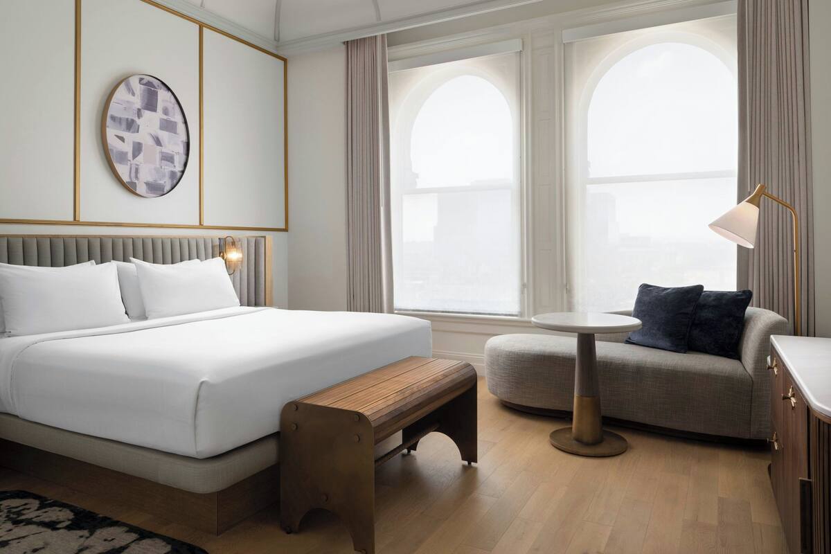 Ein Hotelzimmer mit einem großen Bett, einer kleinen Couch, einem runden Tisch und einer Bank.
