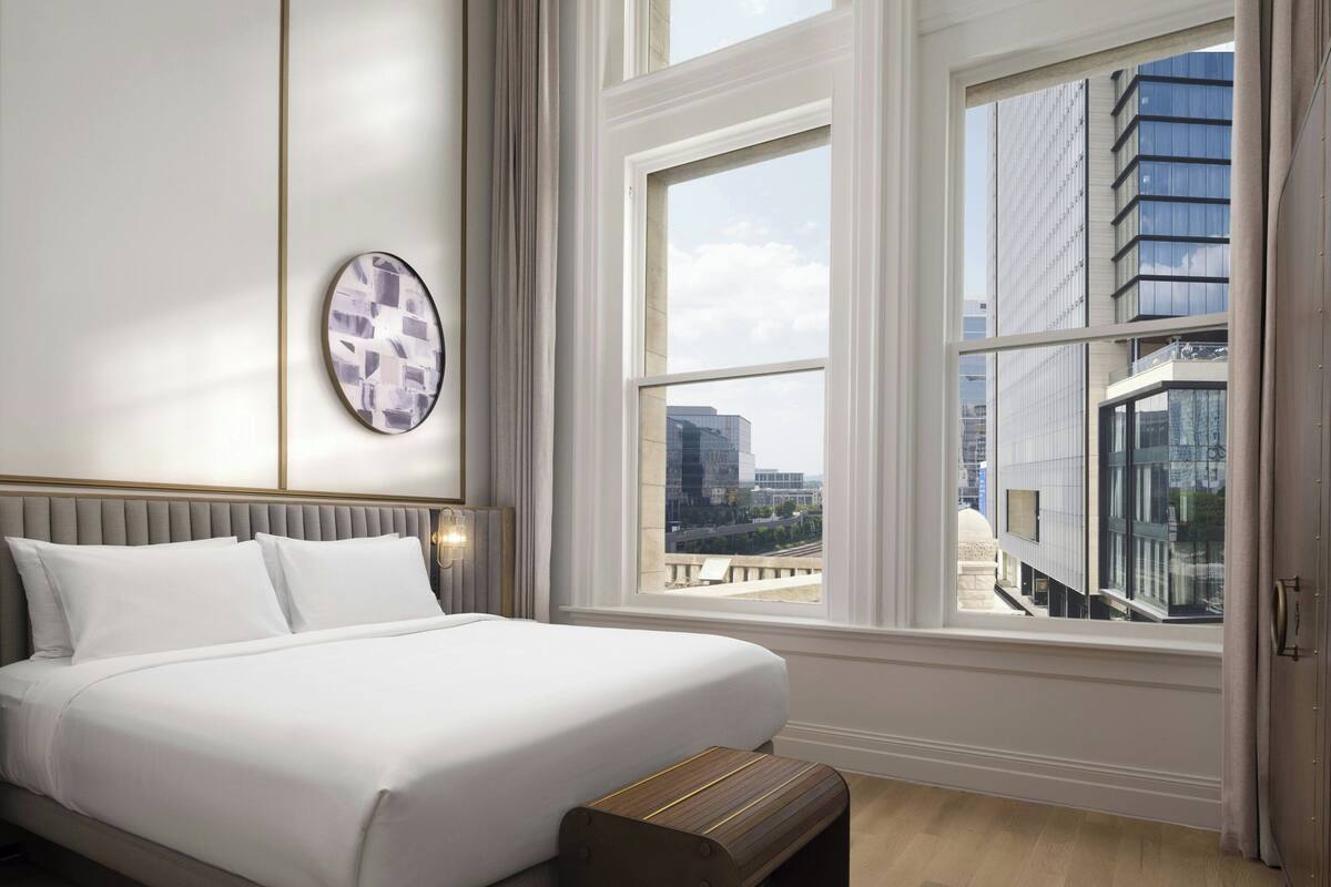 Ein Hotelzimmer mit einem großen Bett, Blick auf die Stadt durch ein großes Fenster und modernem Design.