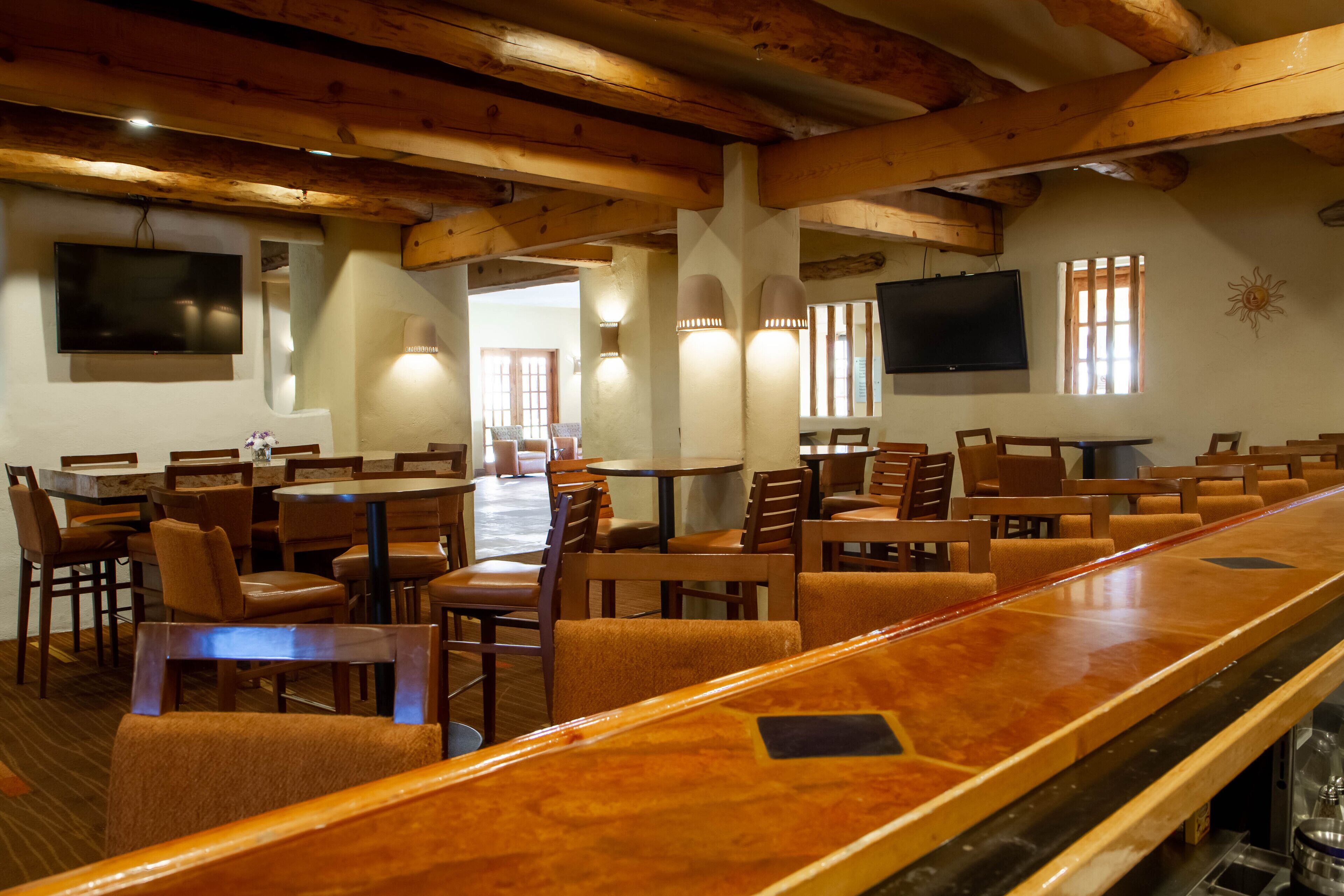 A restaurant with wooden beams, multiple tables and chairs, and wall-mounted televisions.
