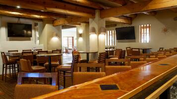 A restaurant with wooden beams, multiple tables and chairs, and wall-mounted televisions.