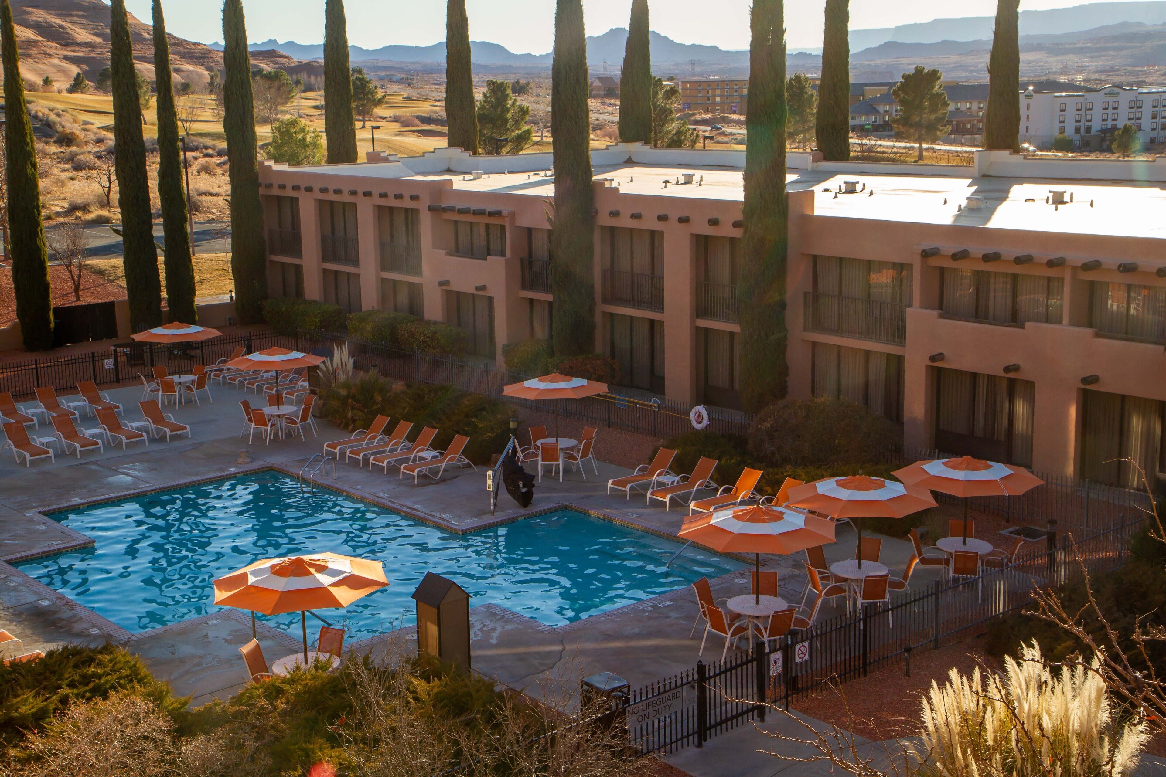 Un hôtel doté d’une piscine entourée de chaises longues et de parasols, d’une terrasse clôturée et offrant une vue sur les montagnes lointaines.