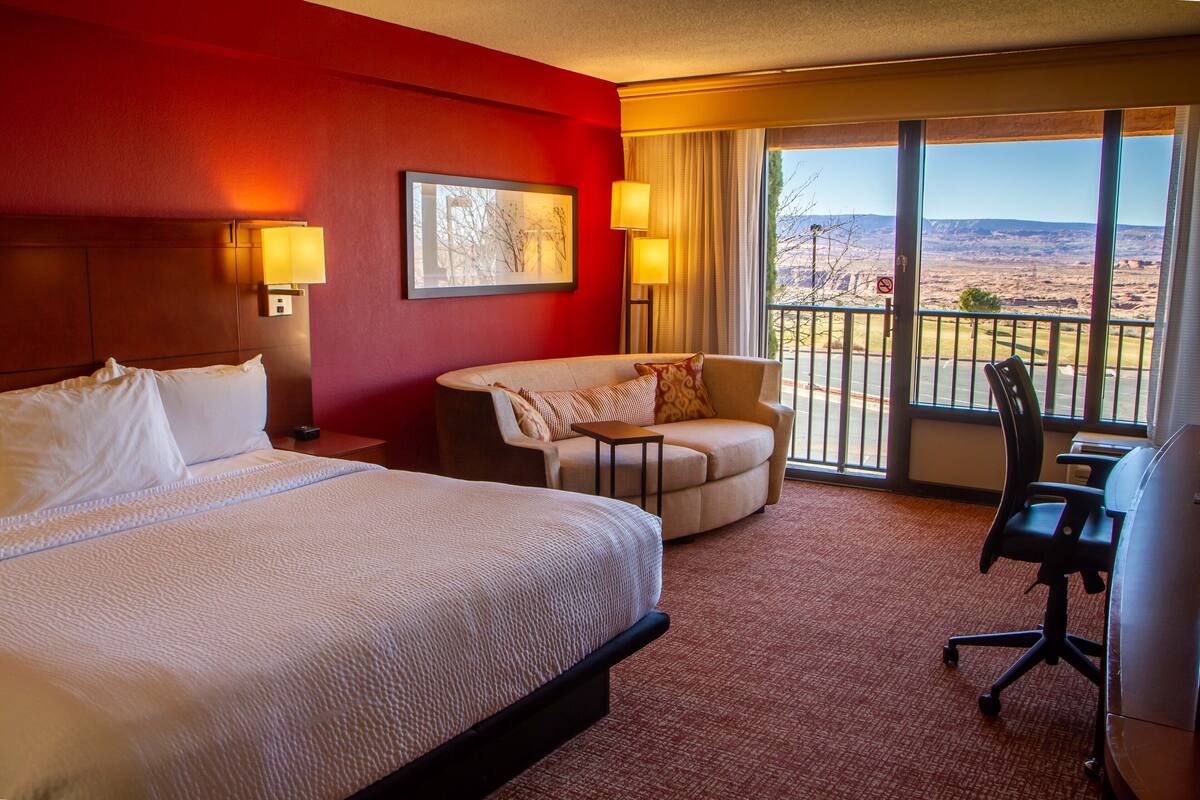 Une chambre d’hôtel avec un grand lit, un canapé, un bureau et une vue sur l’extérieur.