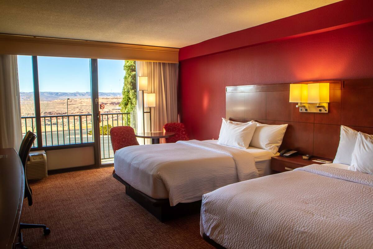 Une chambre d’hôtel avec deux lits, un bureau et une vue sur un paysage désertique.