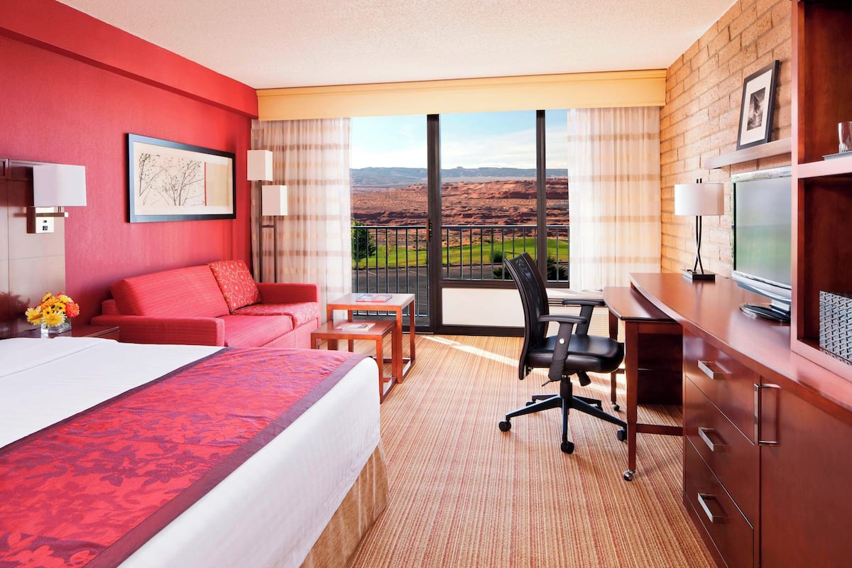 Une chambre d’hôtel dotée d’un grand lit, d’un bureau, d’une chaise, d’une télévision et d’un balcon offrant une vue sur le paysage.