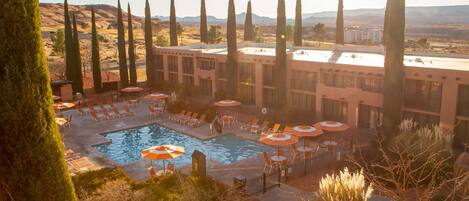 Un hotel con piscina, sillas de descanso y altos cipreses.
