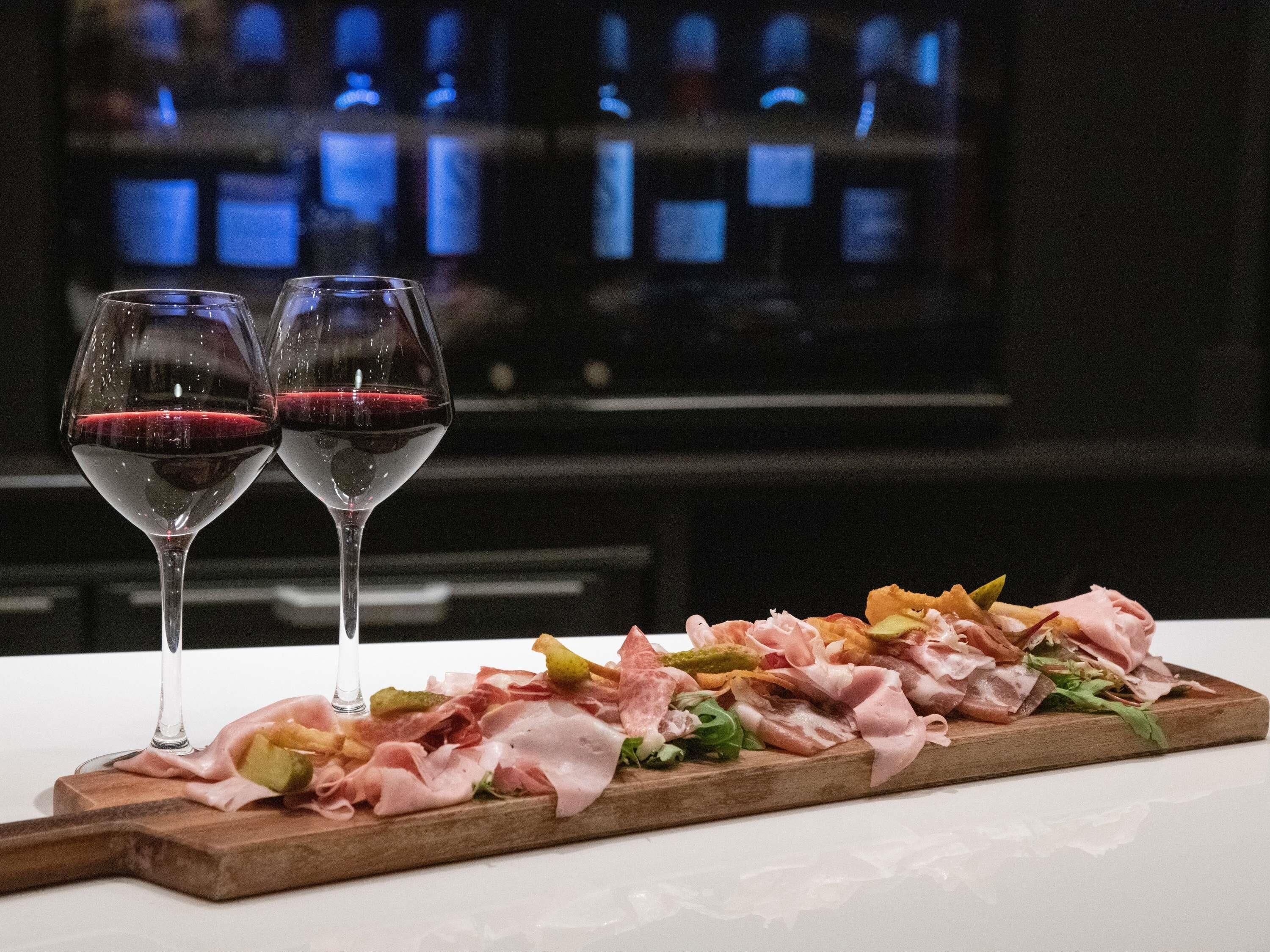 Una tabla de madera con diversos embutidos y una copa de vino tinto.