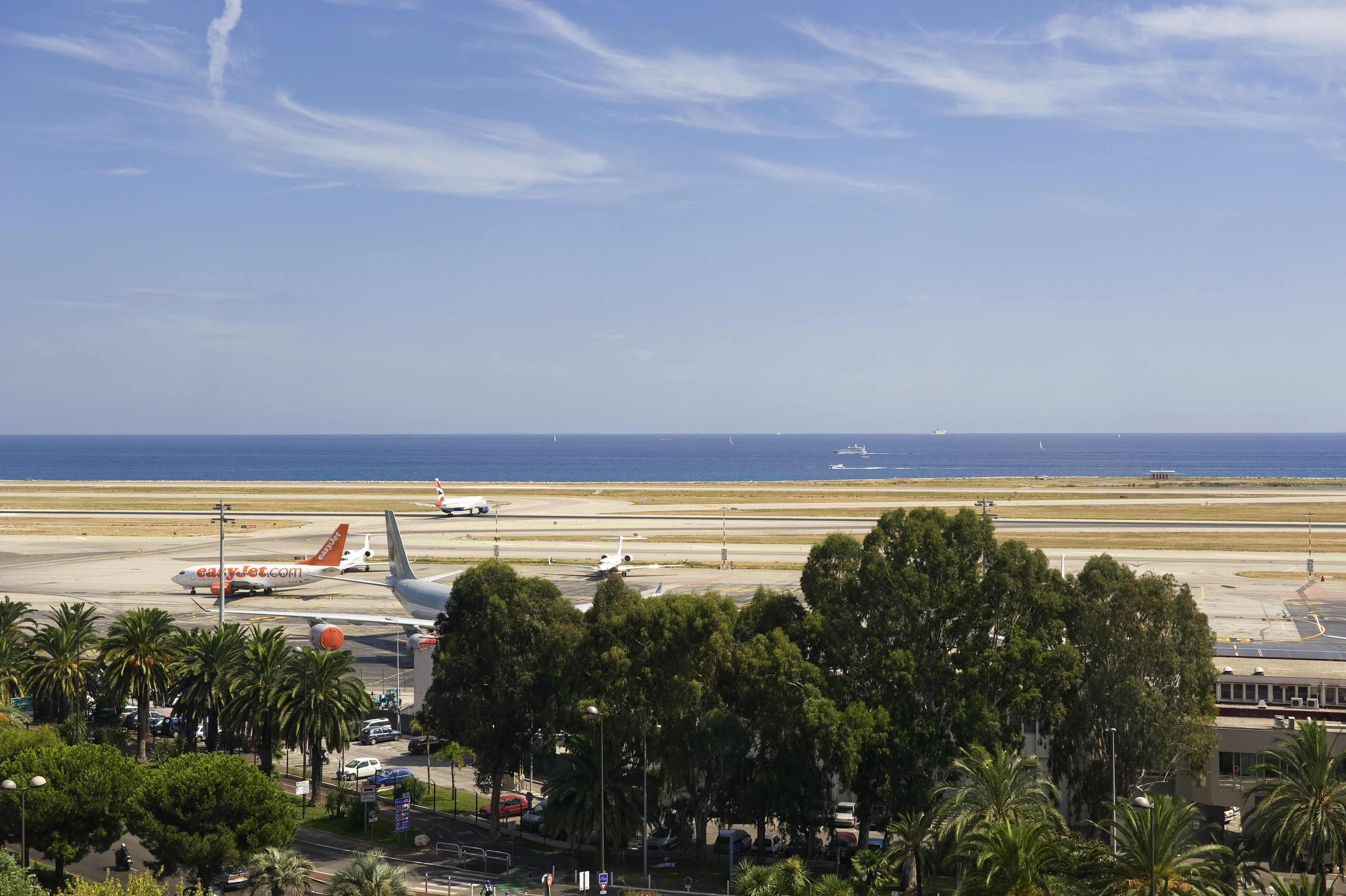 An airport runway with airplanes, palm trees, and a clear sky.
