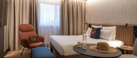 A hotel room with a bed, a desk, a chair, a sofa, and a TV.
