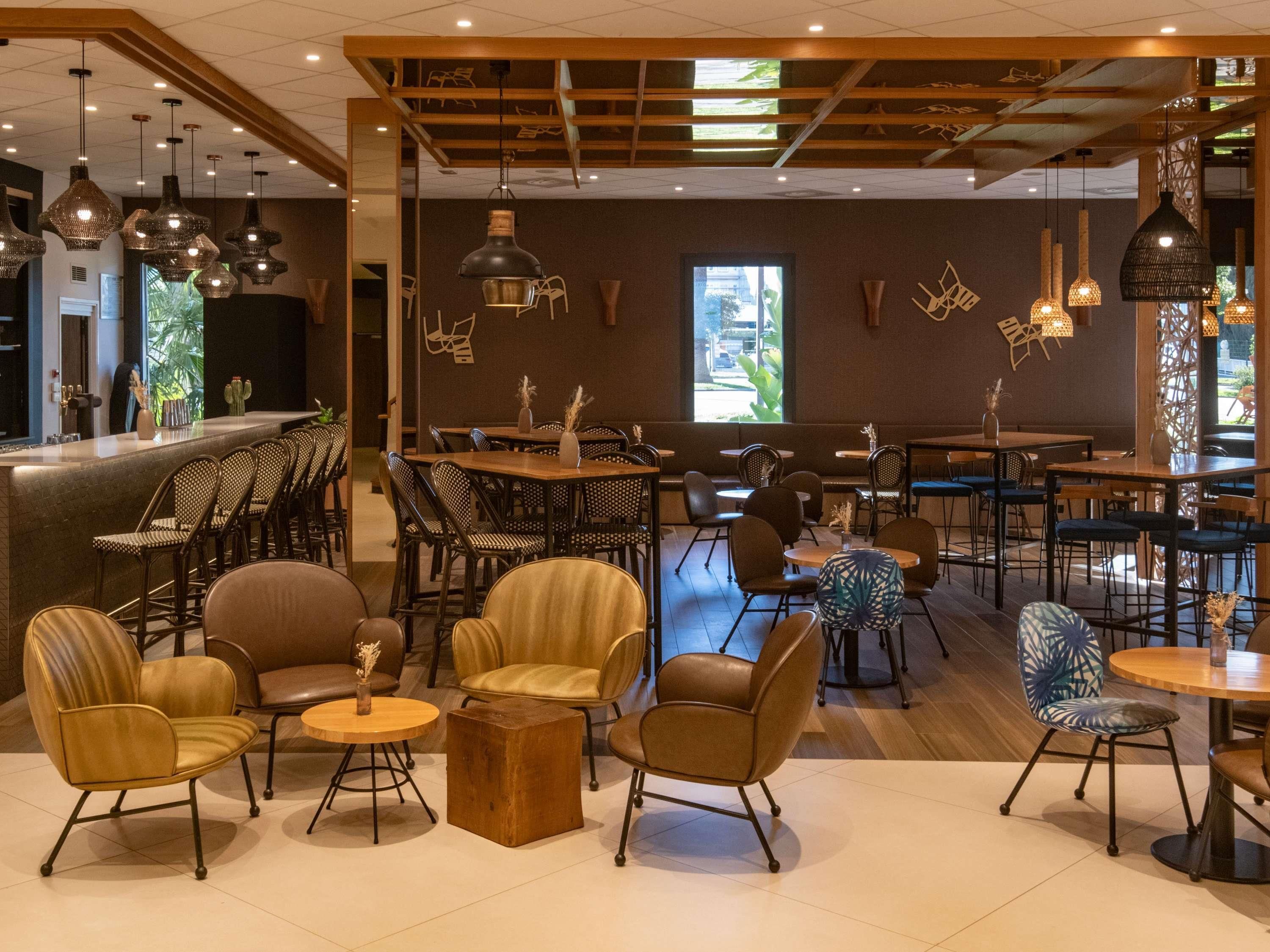 A modern restaurant with a bar area, wooden ceiling, and various seating arrangements including chairs and tables.