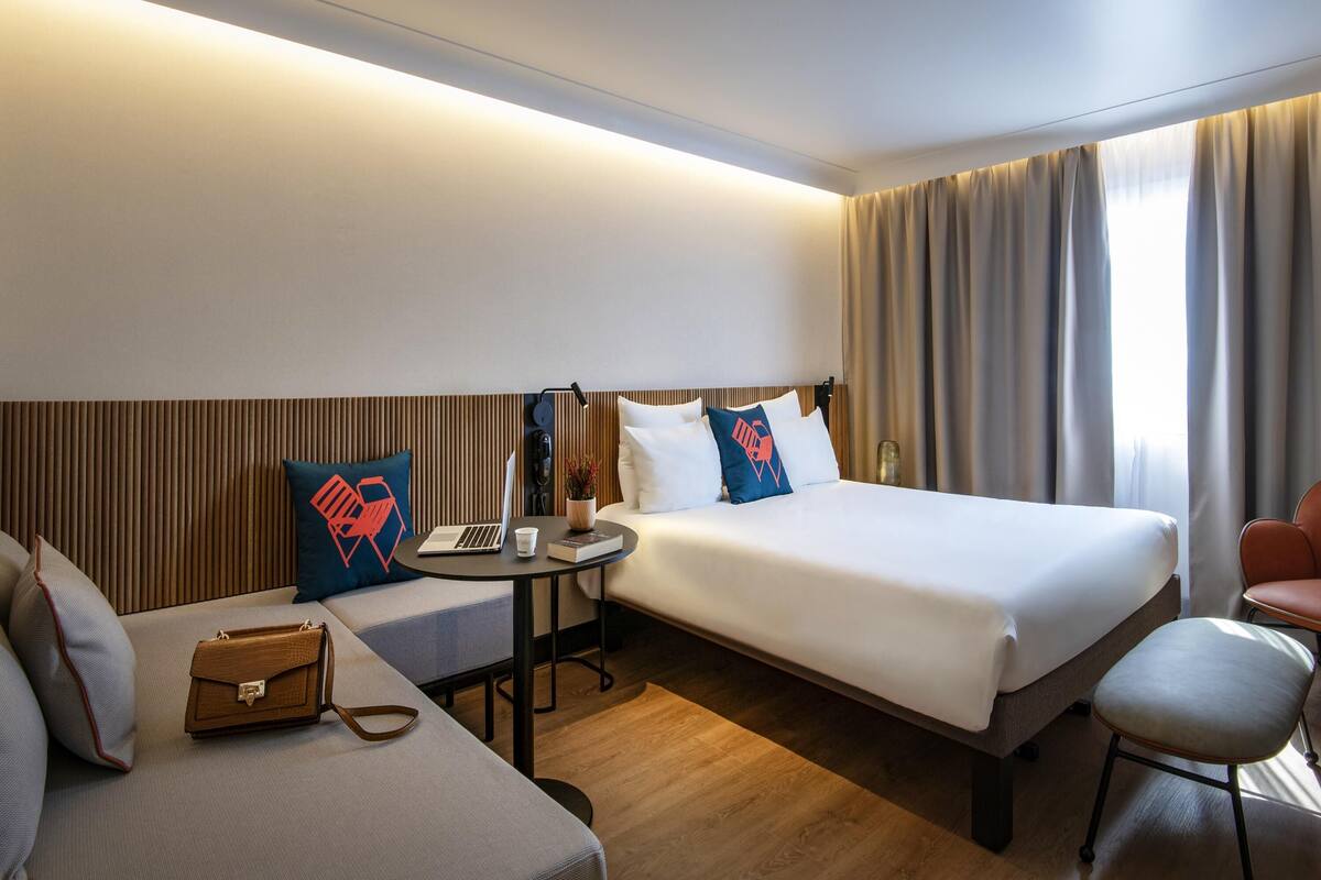 A hotel room with two beds, a desk, a chair, and a sofa.