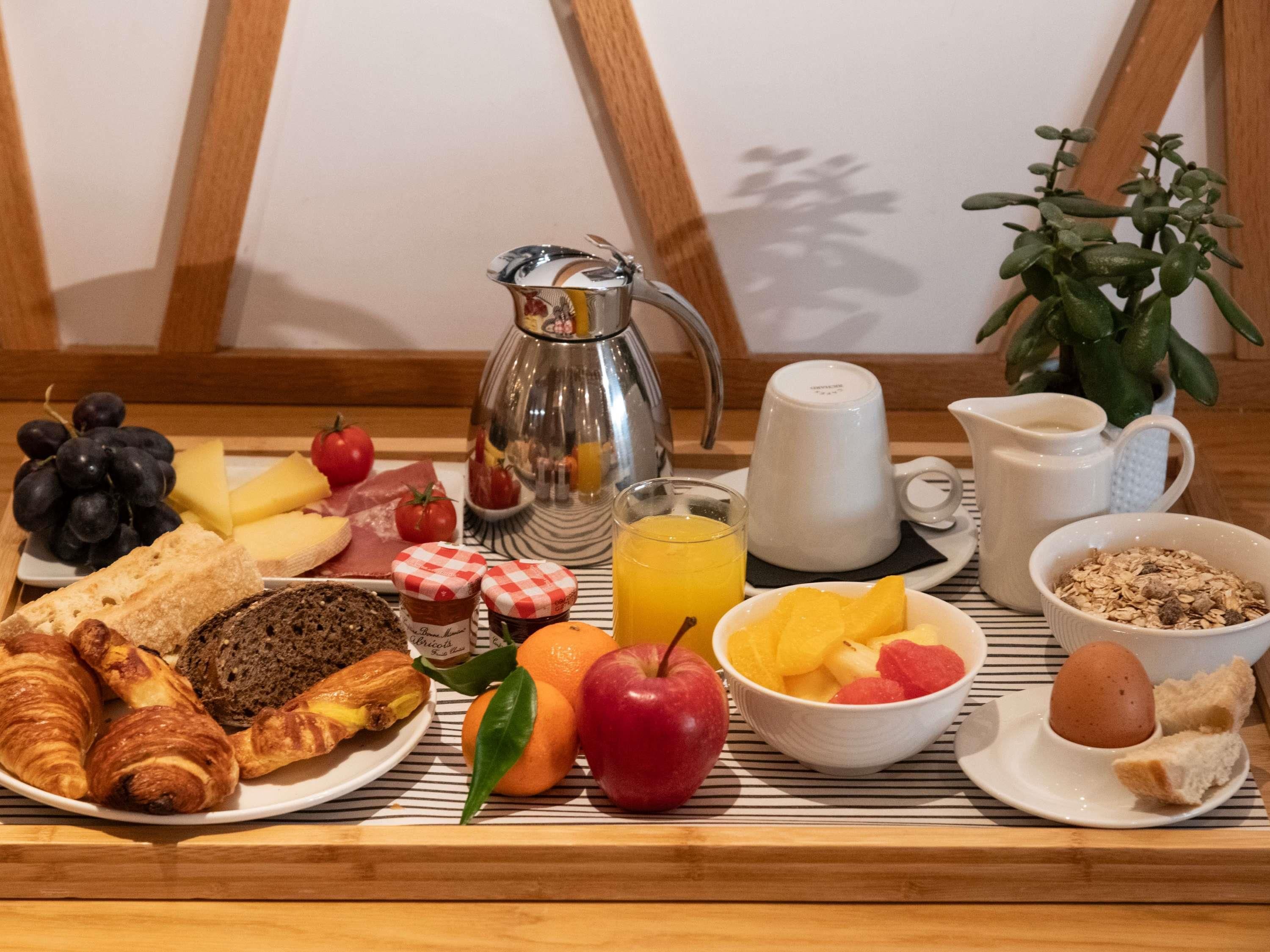 Una mesa de desayuno con croissants, queso, tomates, uvas, pan y una cafetera.