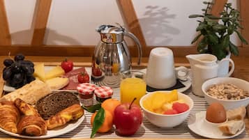 Una mesa de desayuno con croissants, queso, tomates, uvas, pan y una cafetera.