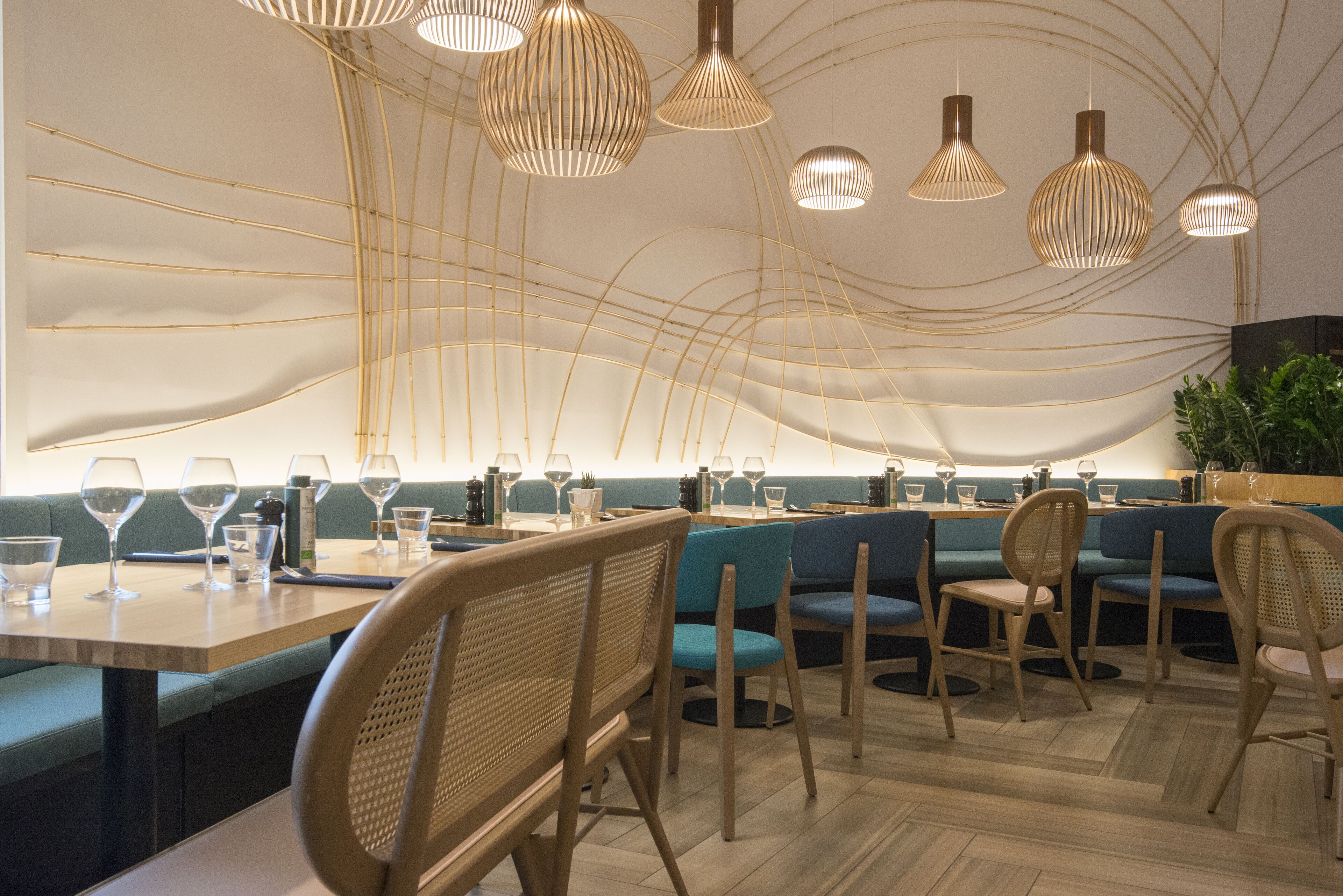 A modern restaurant interior with wooden furniture, hanging pendant lights, and a long dining table.