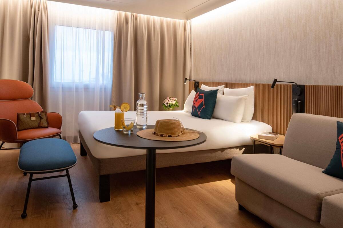 A hotel room with a bed, a chair, a sofa, a small table, and a window with curtains.