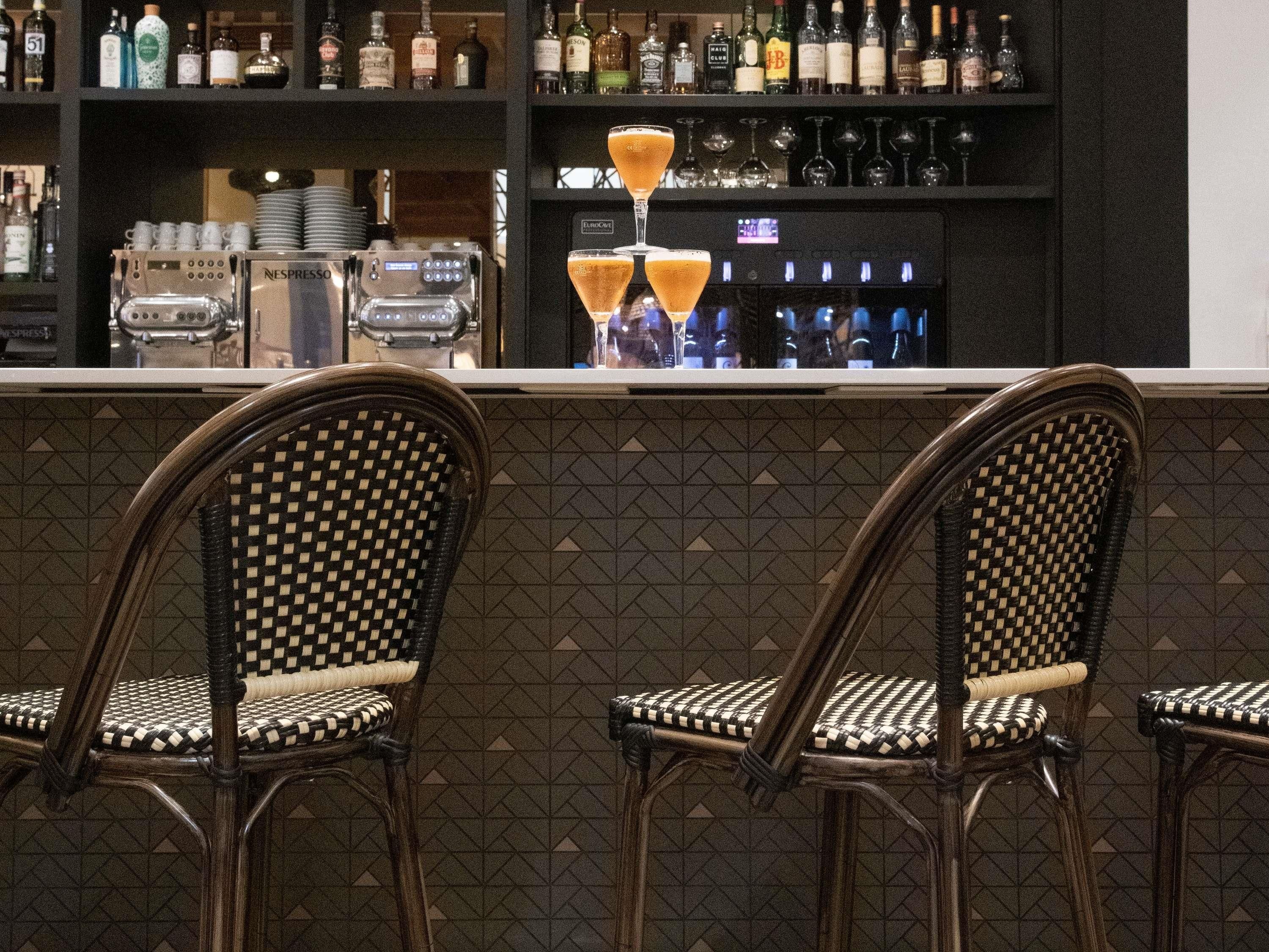 Una zona de bar con mostrador, dos sillas de mimbre, una máquina de Nespresso y una variedad de botellas de licor.