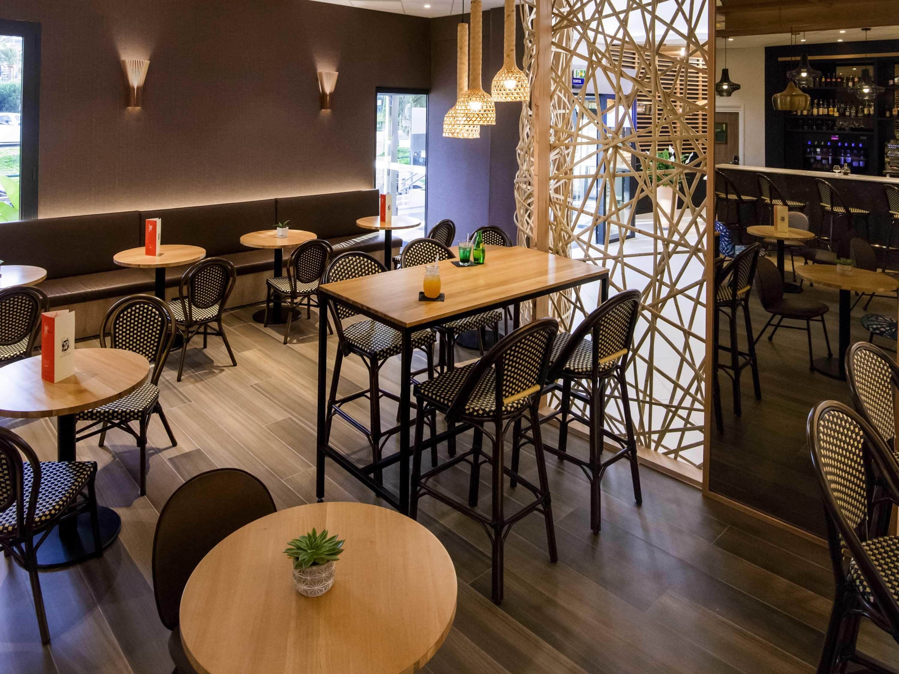 A restaurant with round tables and chairs, a bar area, and a decorative wall.