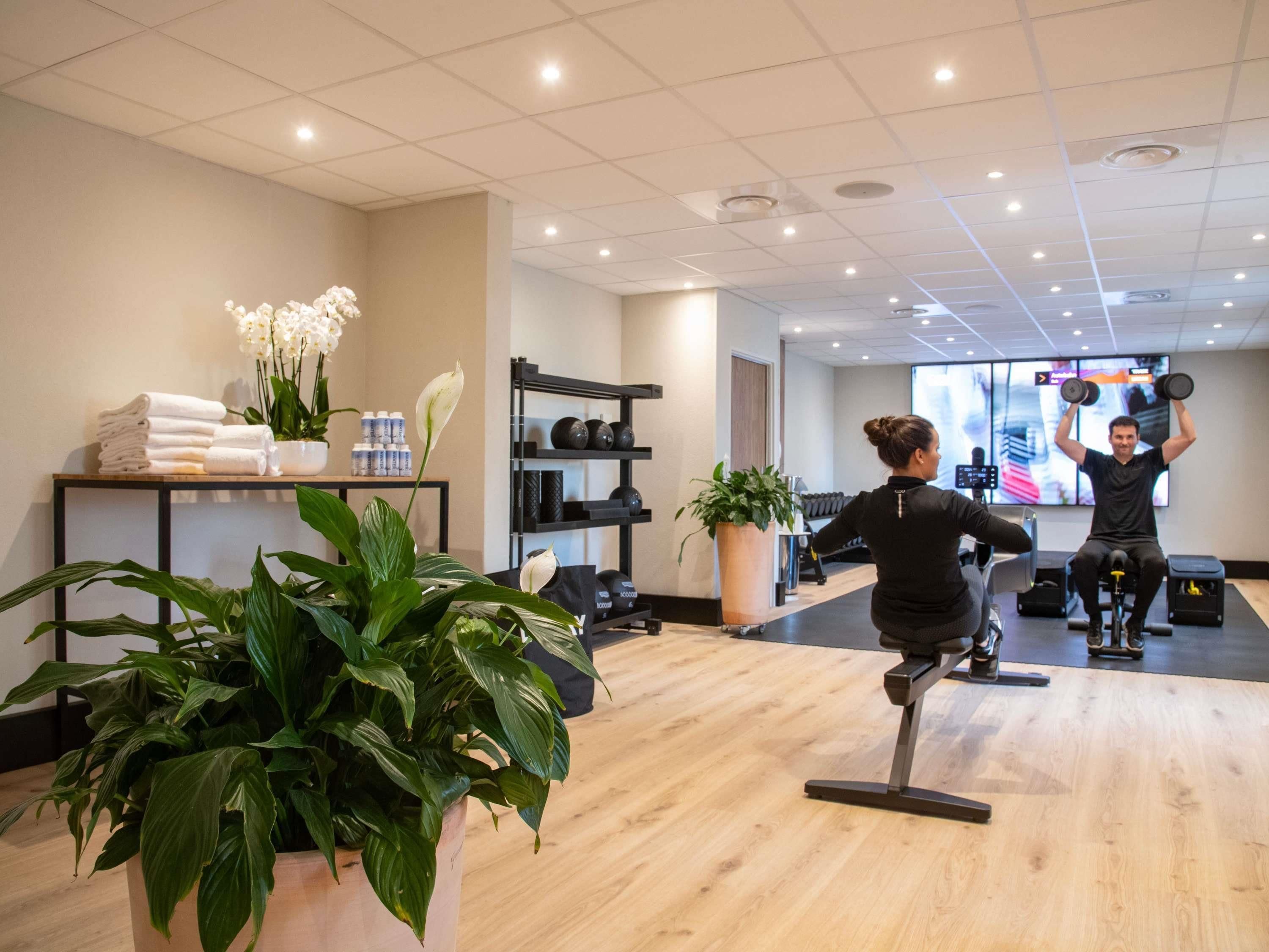 A gym with exercise equipment, a reception desk, and a large potted plant.