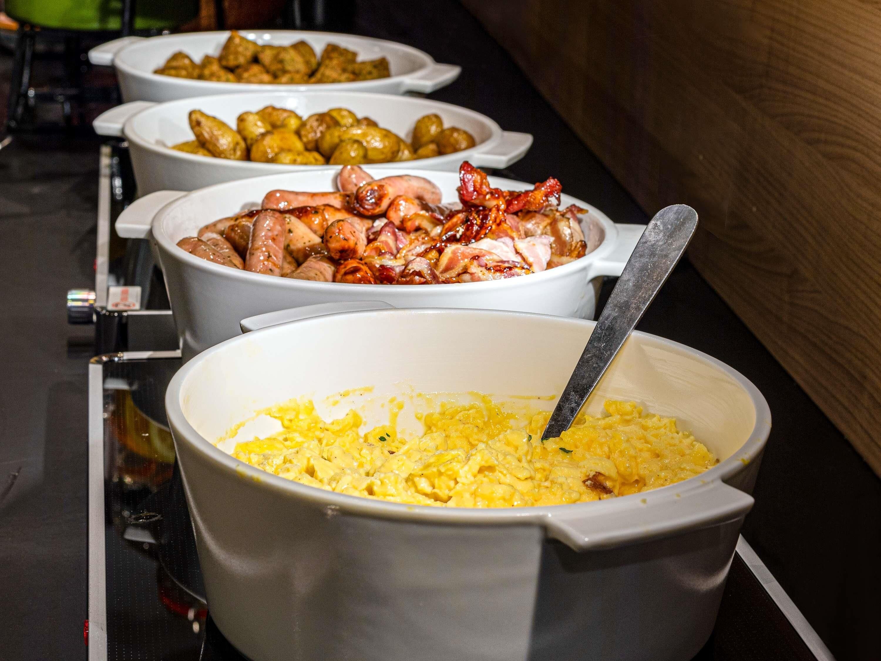 A buffet with various dishes including scrambled eggs, bacon, and roasted potatoes.