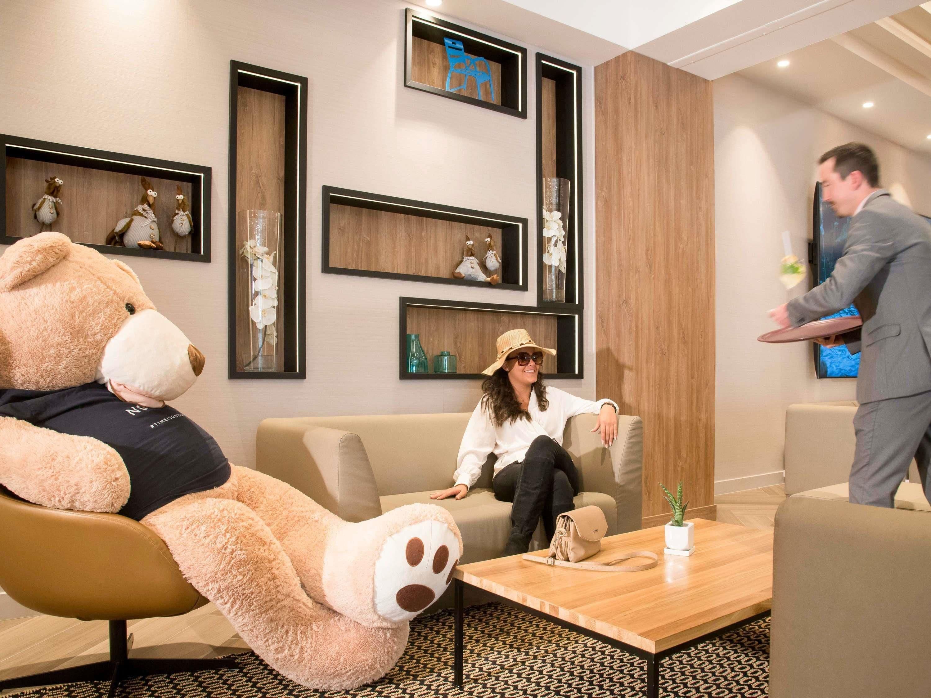 A modern hotel lobby with a large teddy bear, a sofa, a coffee table, and a waiter.