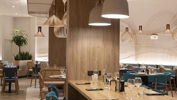 A modern dining area with wooden tables and blue chairs, featuring pendant lighting and a large potted plant.