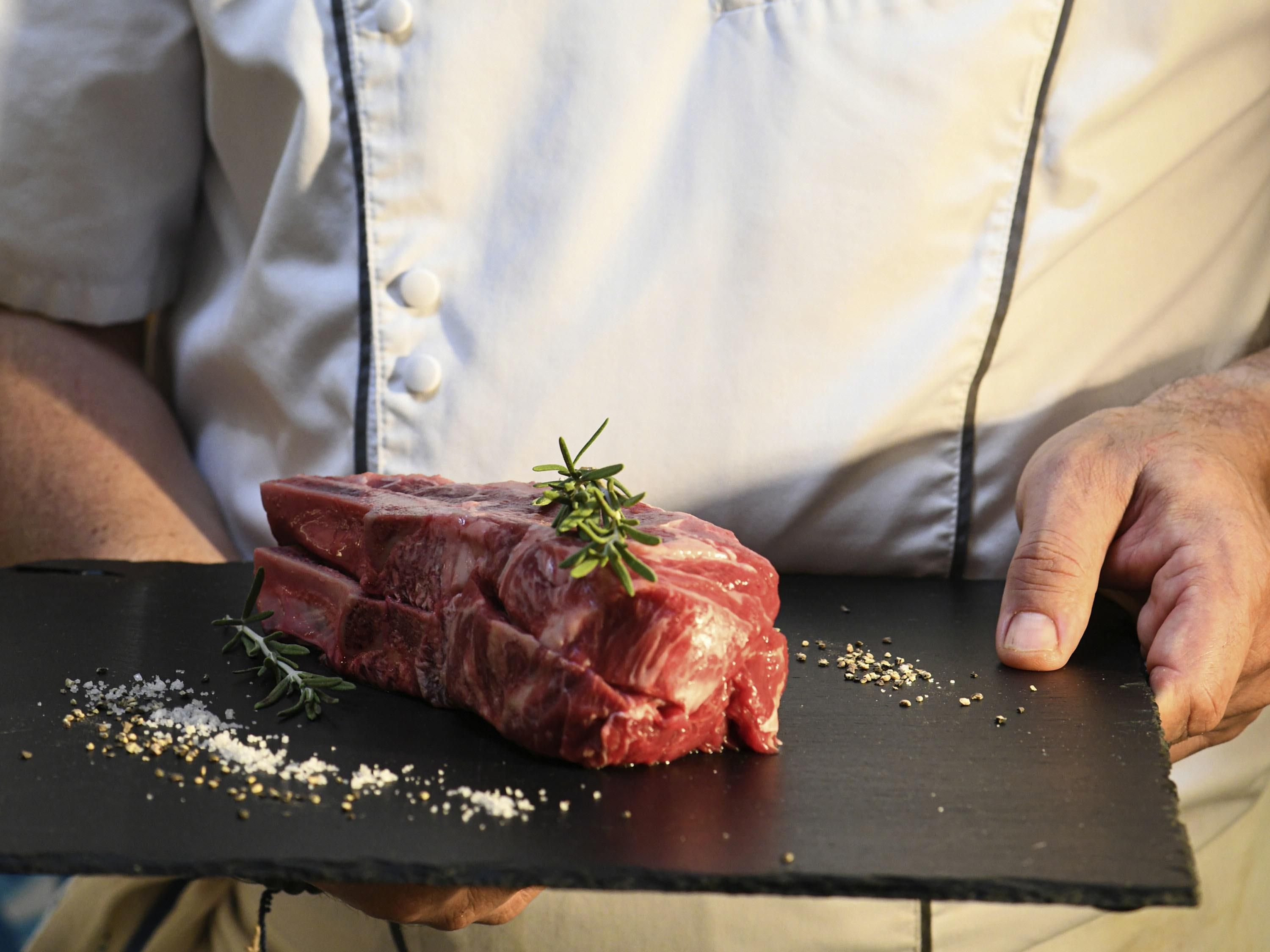 A person holding a black slate board with raw meat and herbs.
