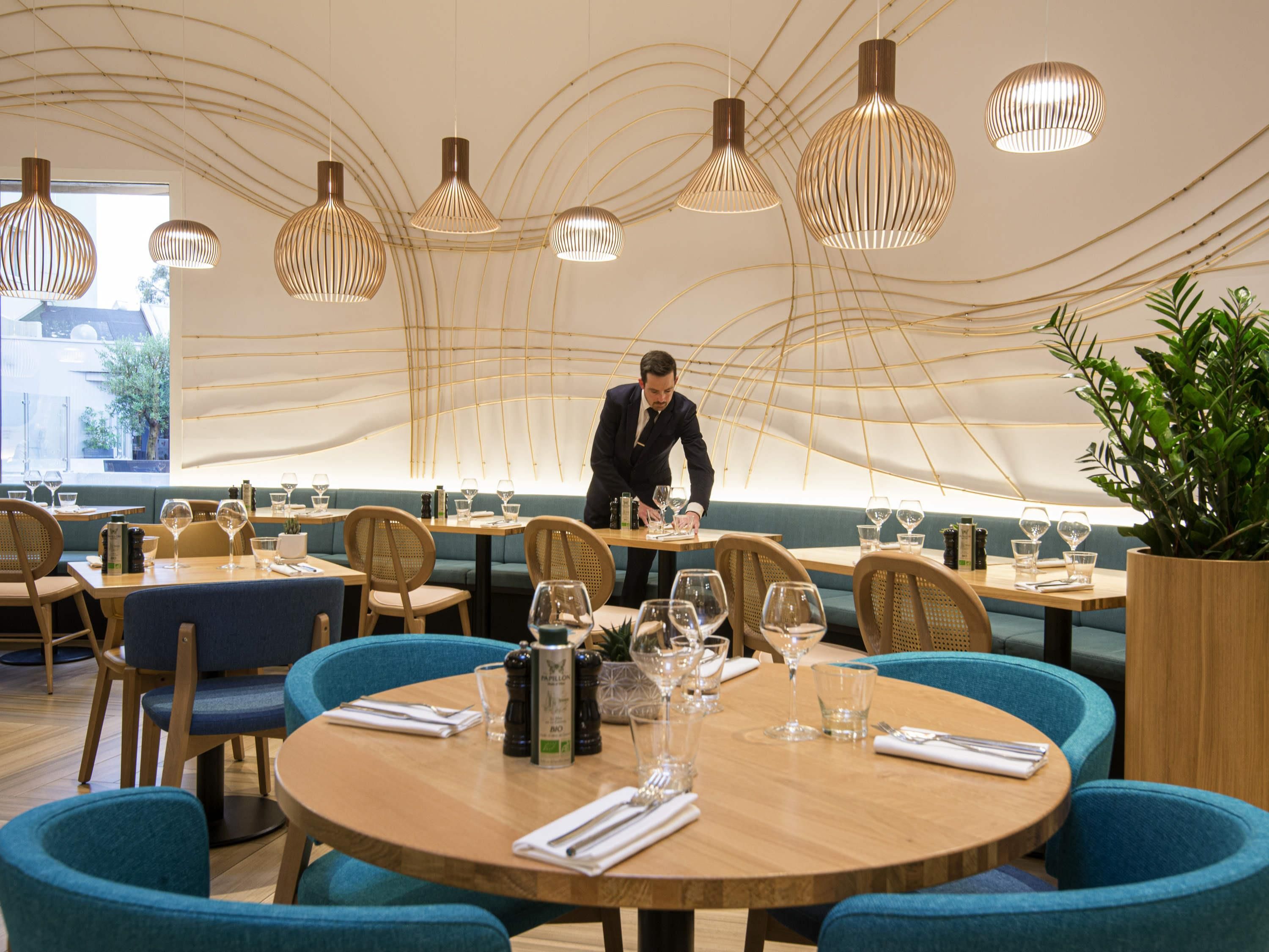 A restaurant with round tables, blue chairs, and hanging pendant lights.