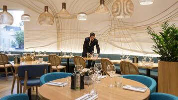 A restaurant with round tables, blue chairs, and hanging pendant lights.