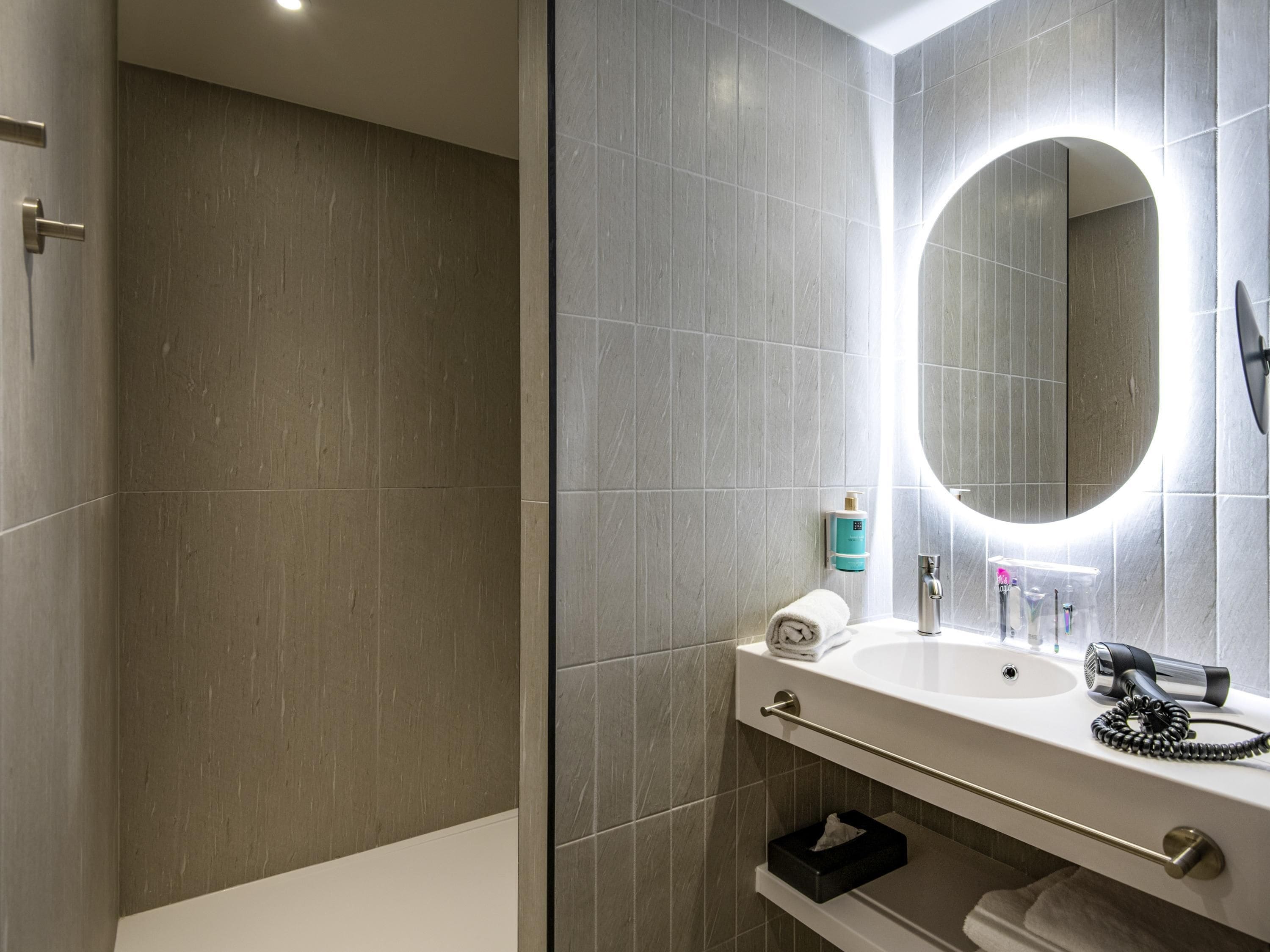 A modern bathroom with a large mirror, a sink, a towel rack, and a hairdryer.