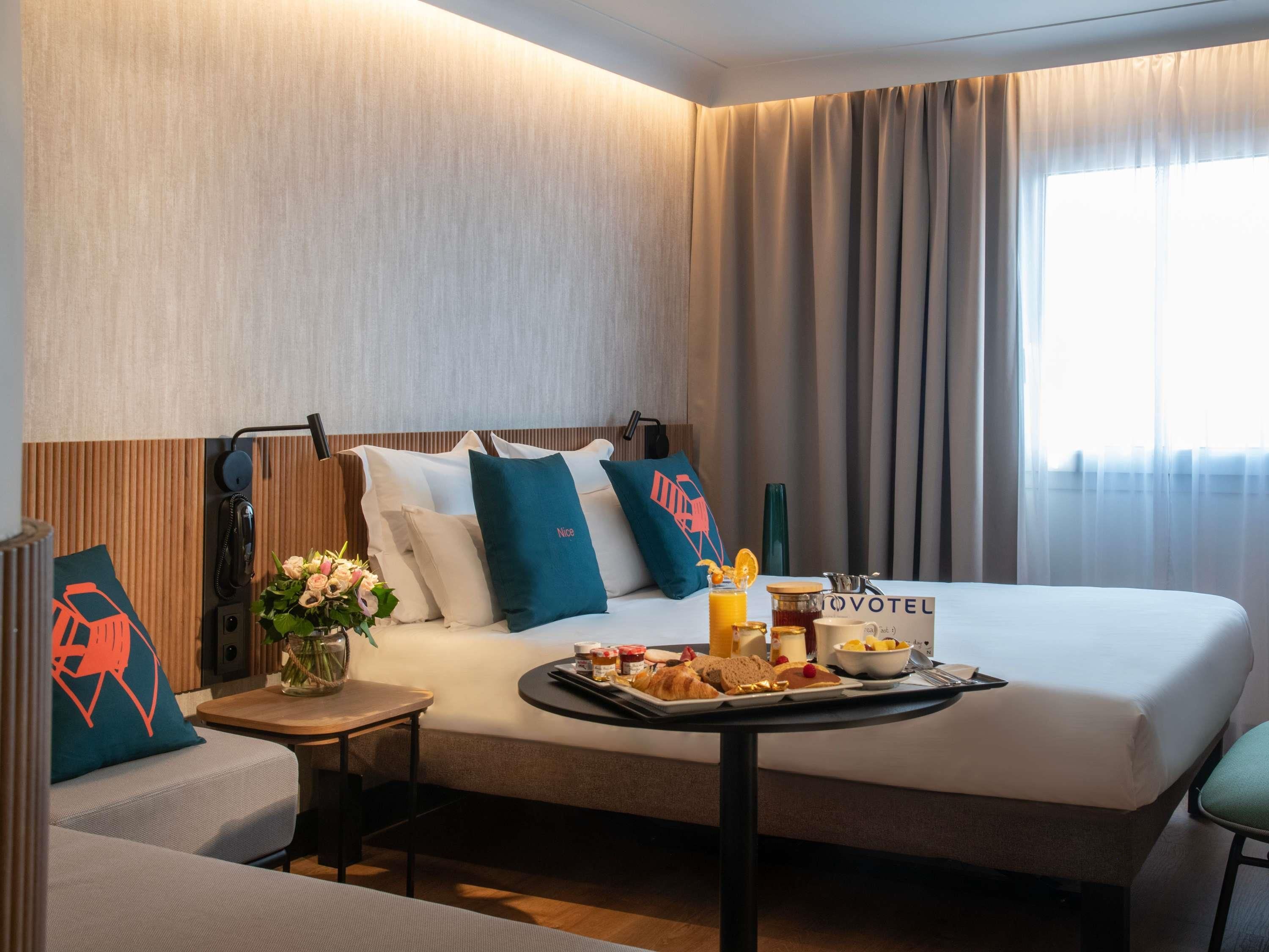 Hotellihuone, jossa on sänky, pieni aamiaispöytä, puhelin ja seinään kiinnitetty valaisin.