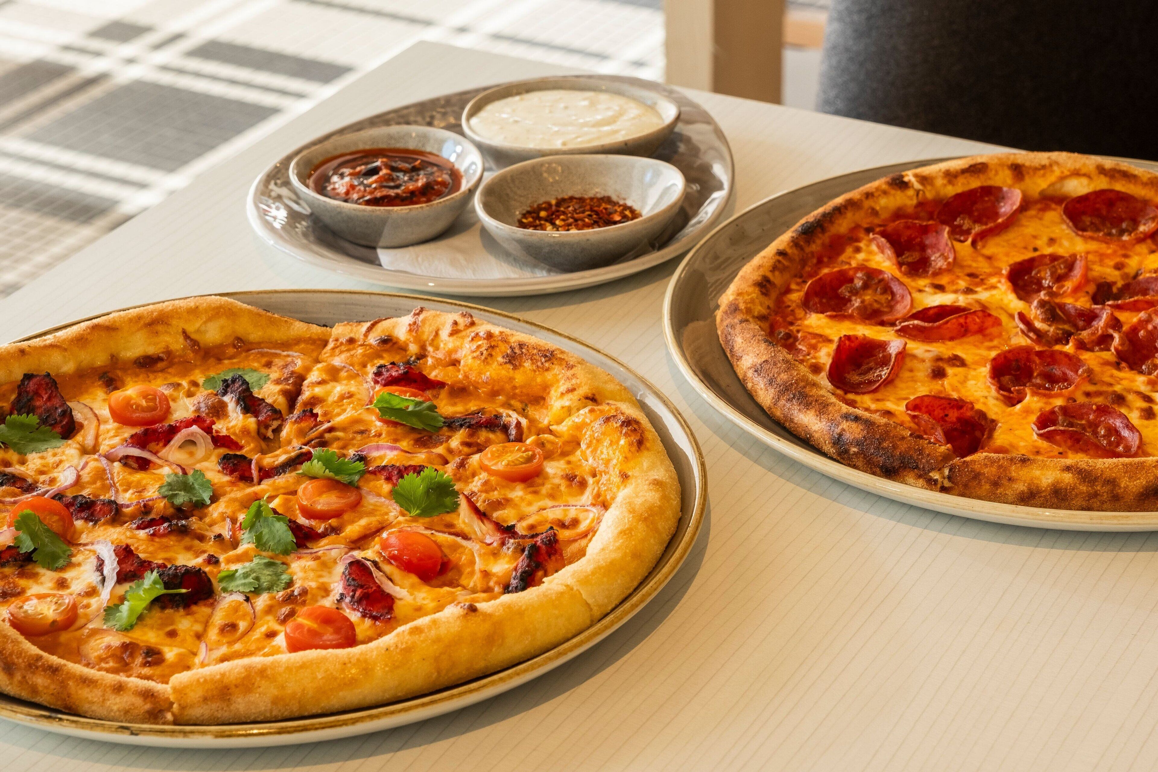 Dos pizzas sobre una mesa con un periódico y una taza de café.
