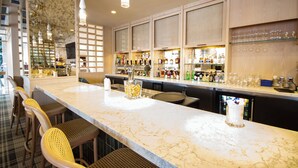 A bar area with a marble countertop, bar stools, and a variety of bottles and glasses.