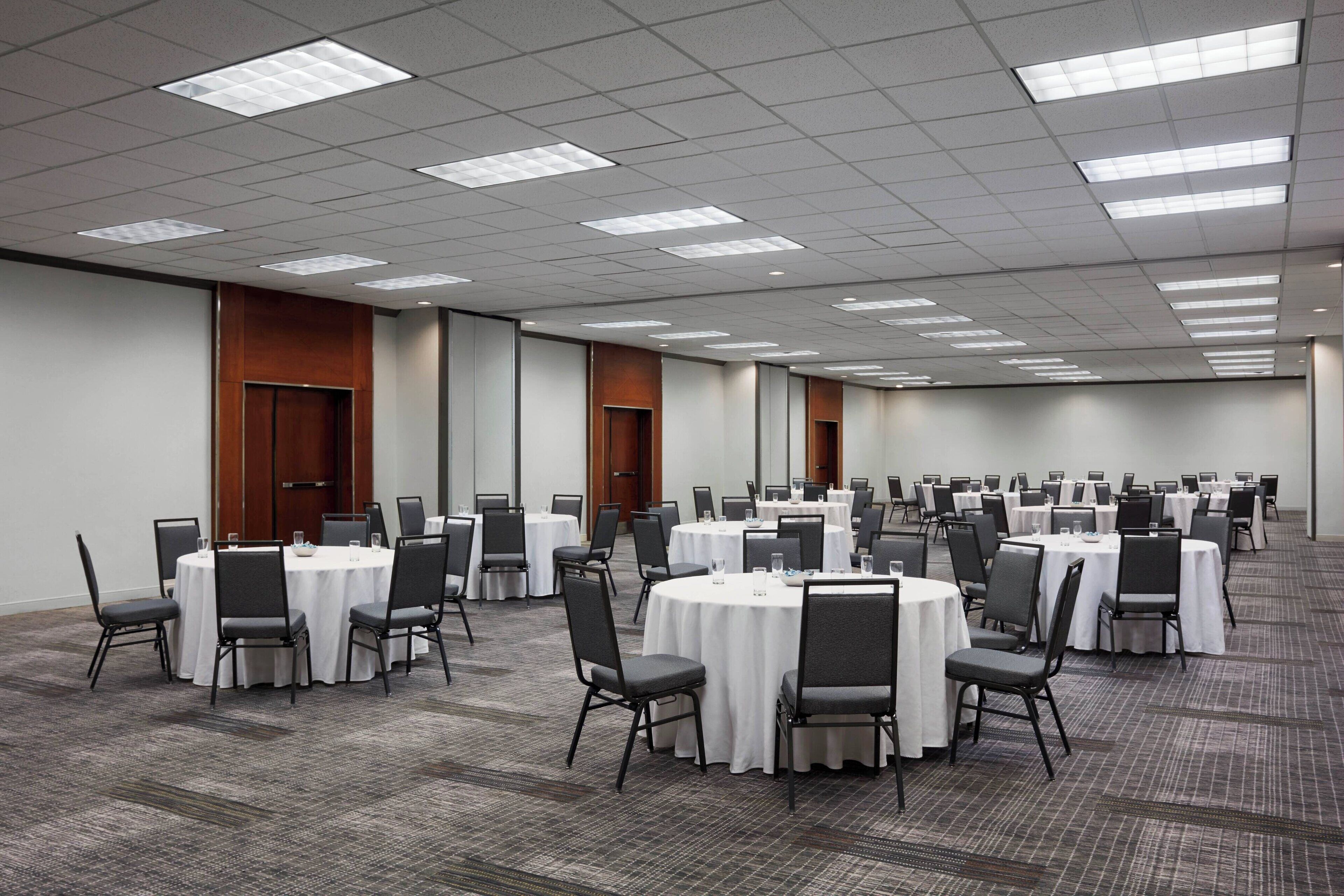 A large conference room with multiple round tables and chairs, carpeted flooring, and recessed lighting.