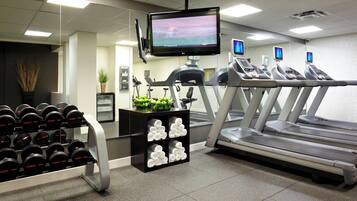 A gym with treadmills, dumbbells, and a TV screen.