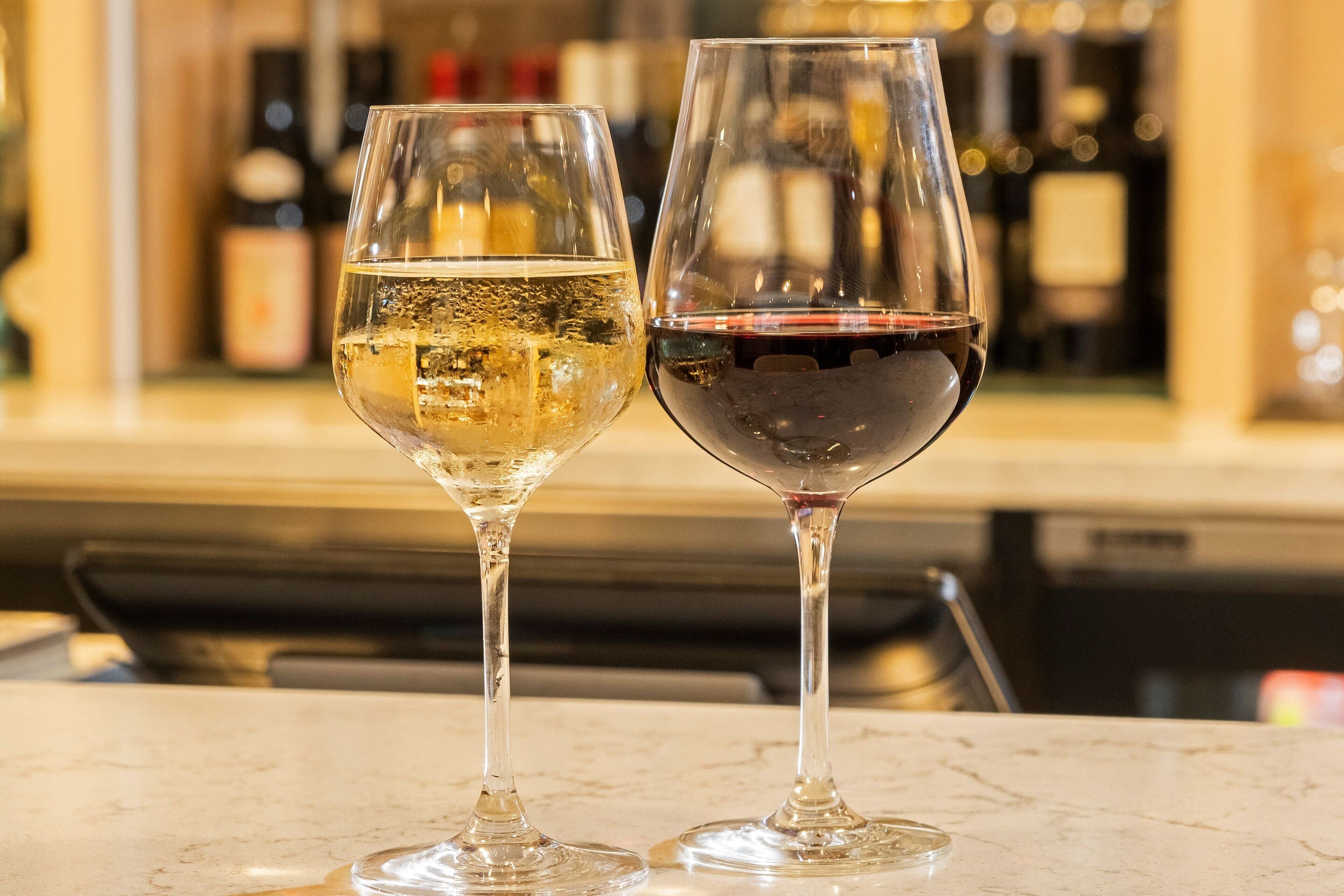 Dos copas de vino sobre una encimera de mármol, con un fondo desenfocado de botellas.