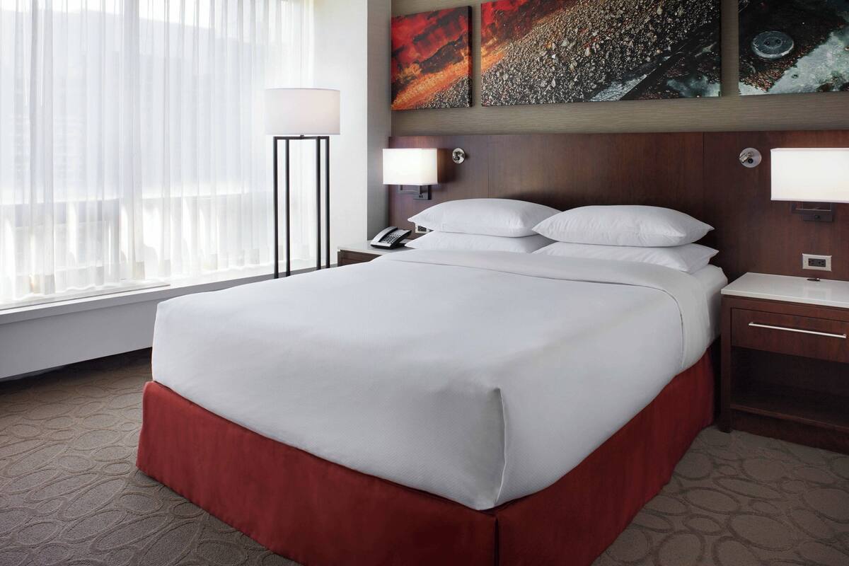 A hotel room with a large bed, a bedside table with a lamp, a nightstand, and artwork on the wall.