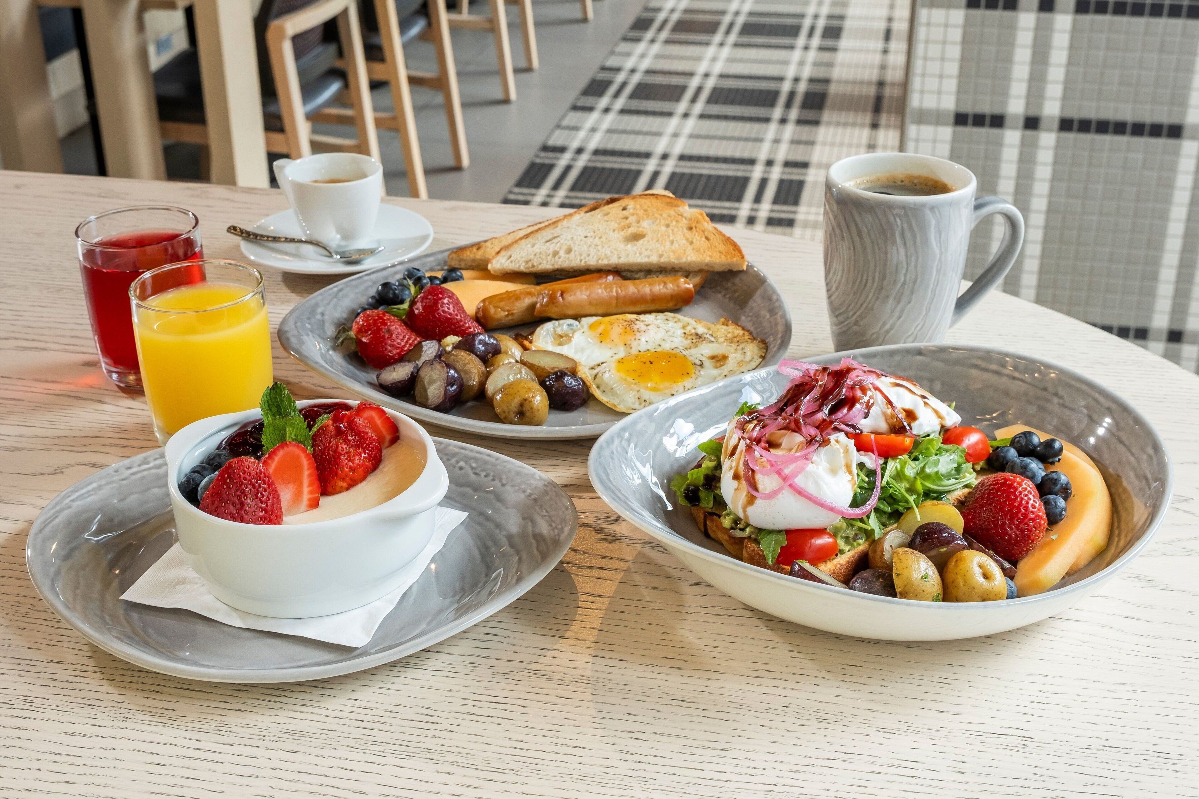 A breakfast table with a variety of dishes including toast, eggs, sausages, and a salad with fruits and a poached egg on top.