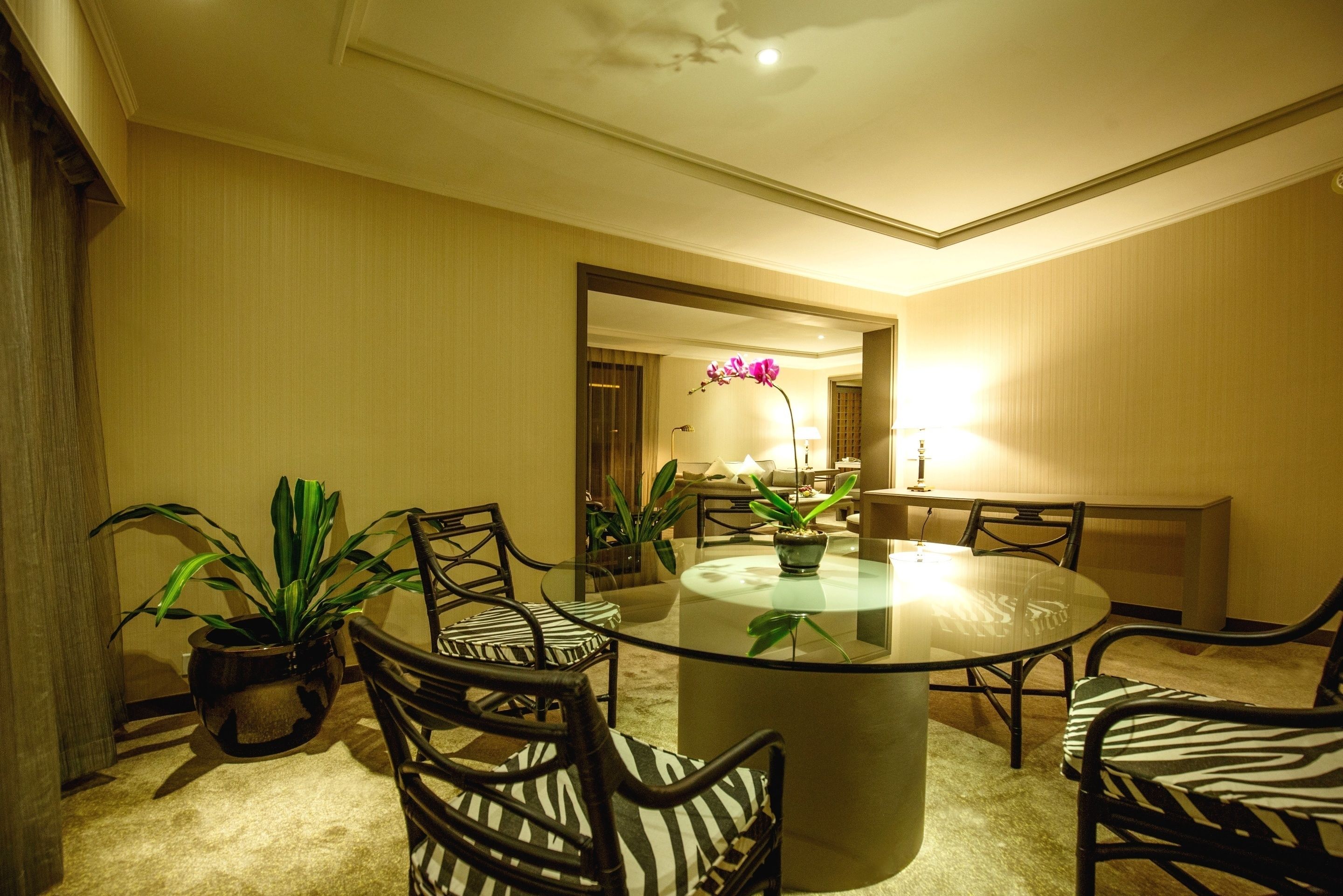 A round glass table surrounded by zebra-patterned chairs in a well-lit room with beige walls and a ceiling light.