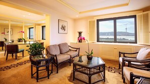 A well-lit living room with a sofa, chairs, a coffee table, and a view of a tower through a large window. - Regency Art Hotel Macau (Taipa)
