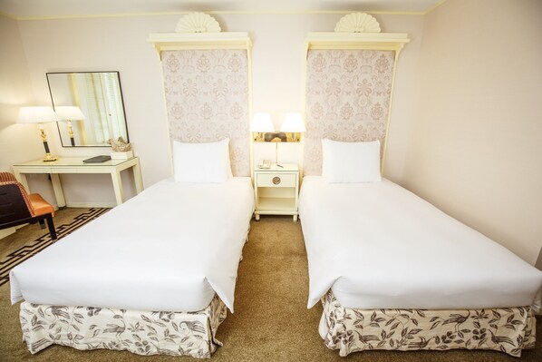 A hotel room with two single beds, a desk with a chair, a nightstand with lamps, and a mirror. - Regency Art Hotel Macau (Taipa)
