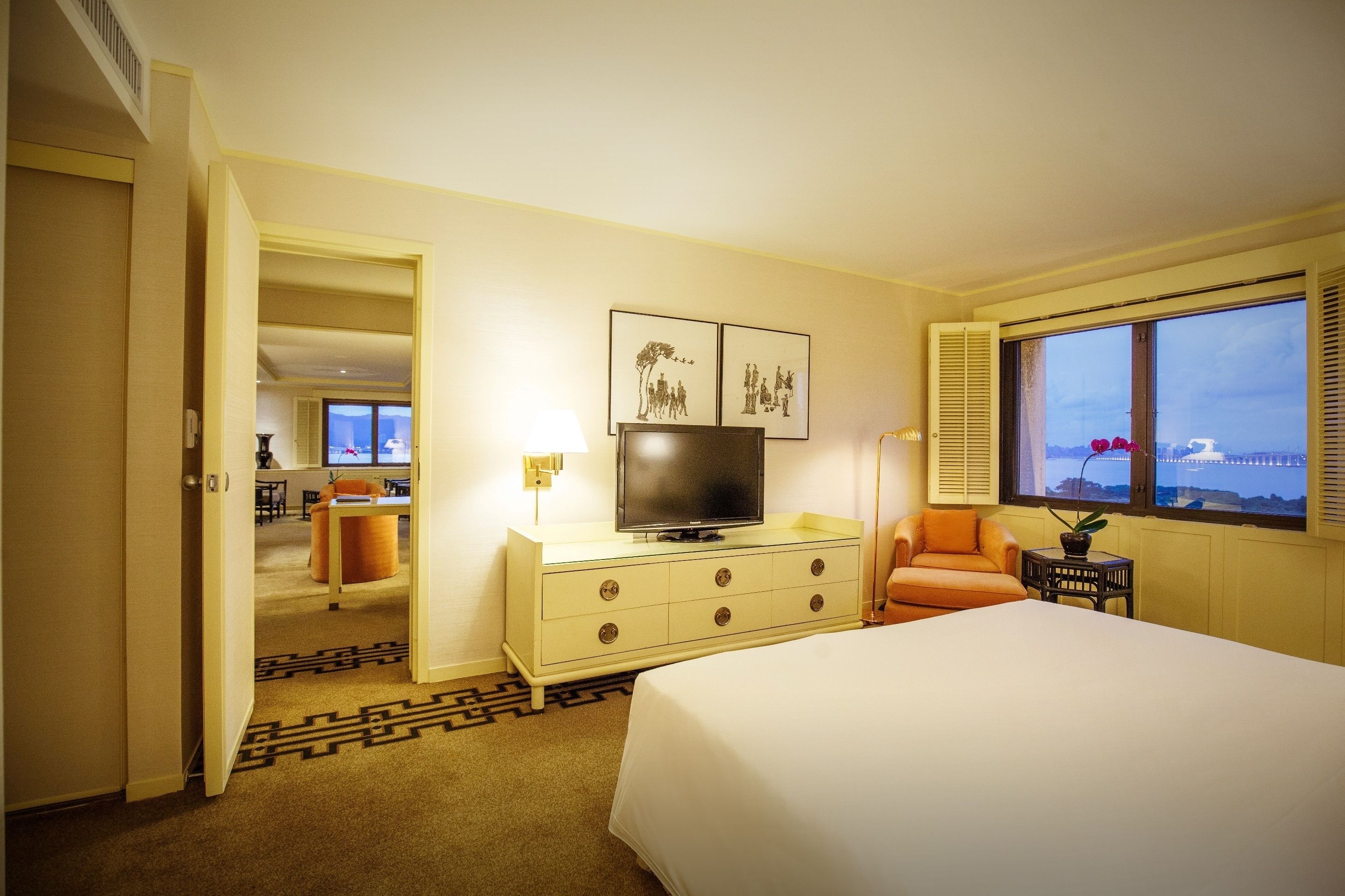 Une chambre d’hôtel avec un lit, un téléviseur posé sur une commode, un bureau avec une lampe et une fenêtre donnant sur un paysage.