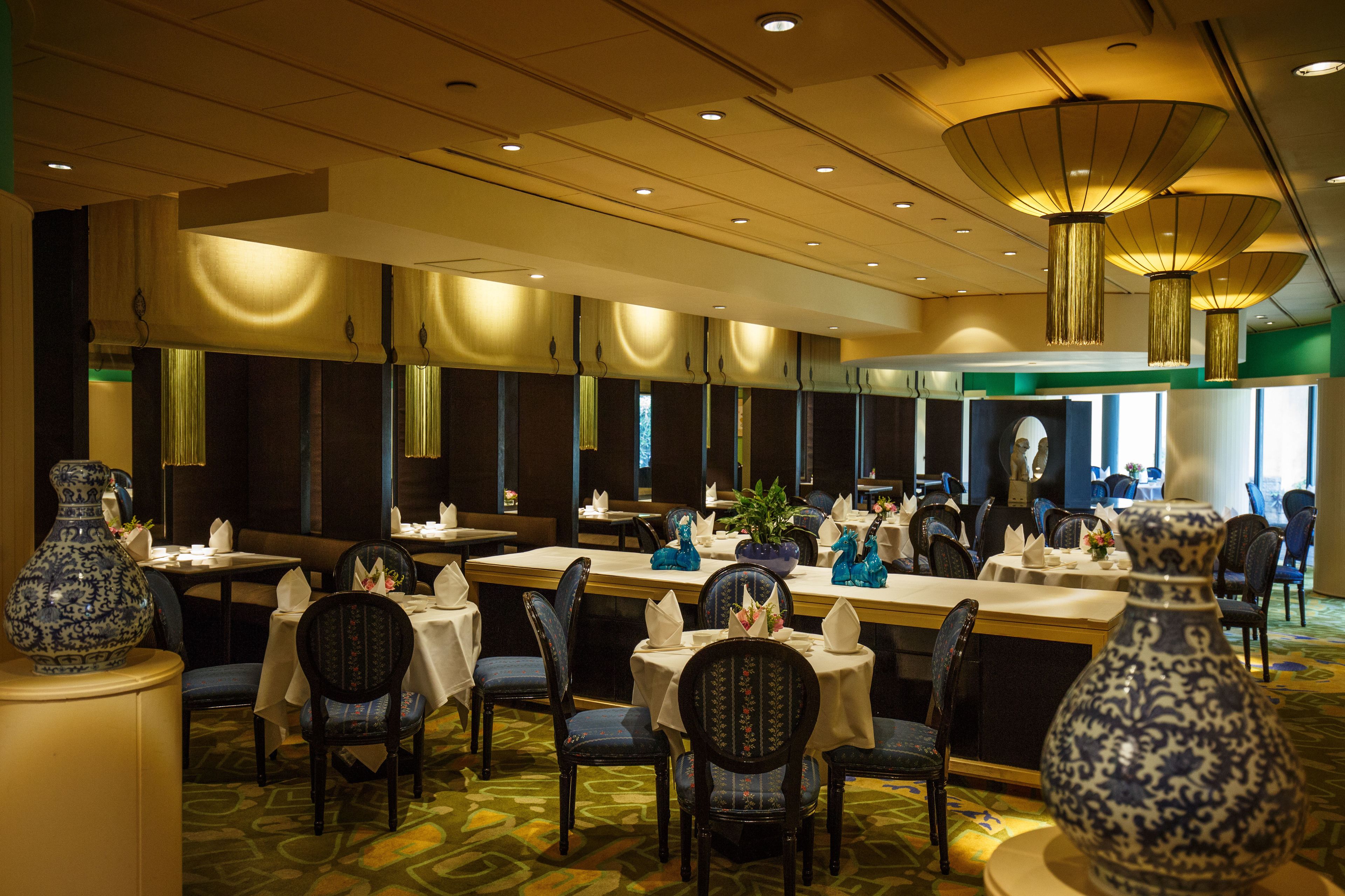 A restaurant with multiple tables and chairs, a large vase, and a ceiling with recessed lighting.
